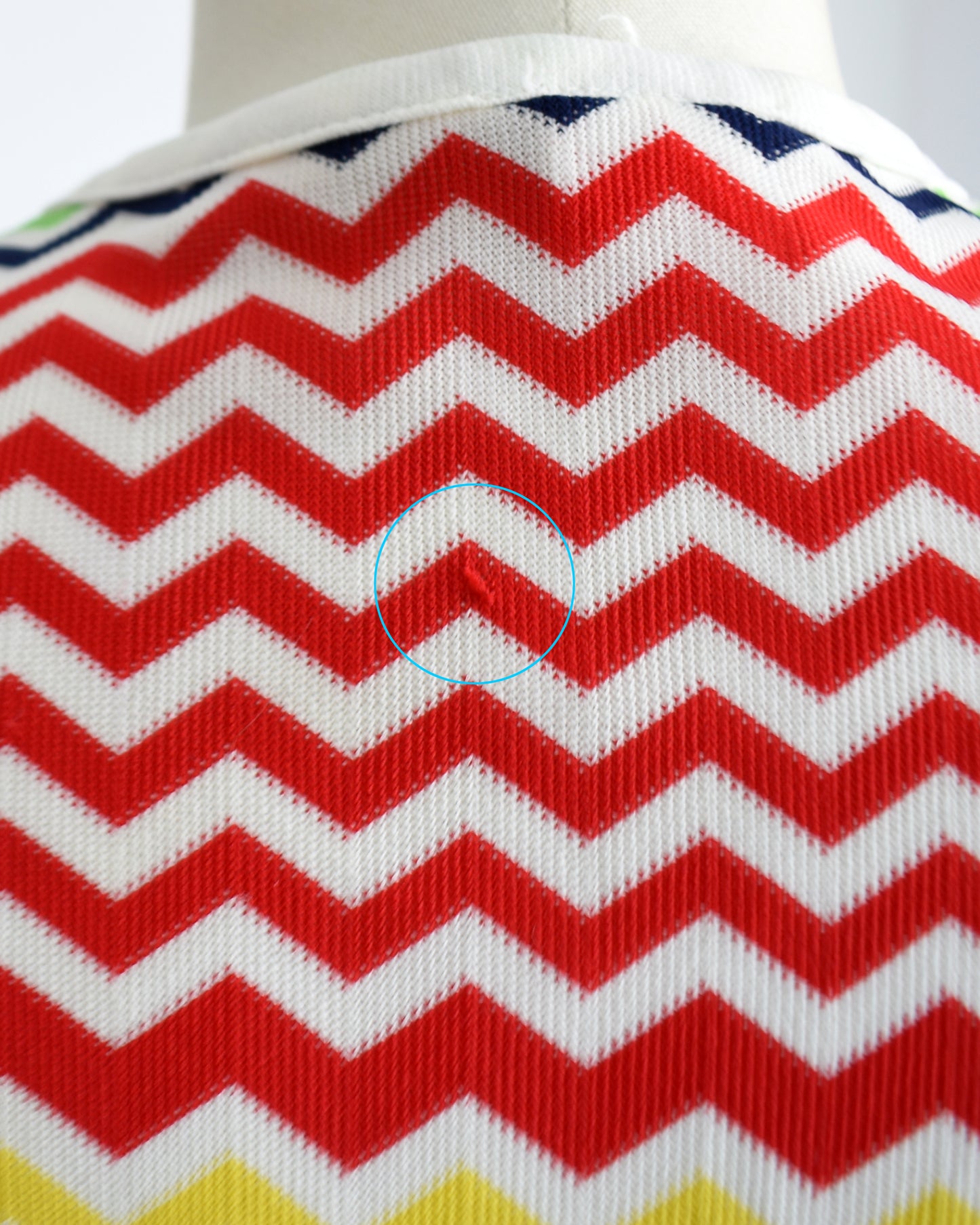 close up of a small pull on the back of a vintage 1970s colorful zigzag patterned sleeveless top on a mannequin against a white background