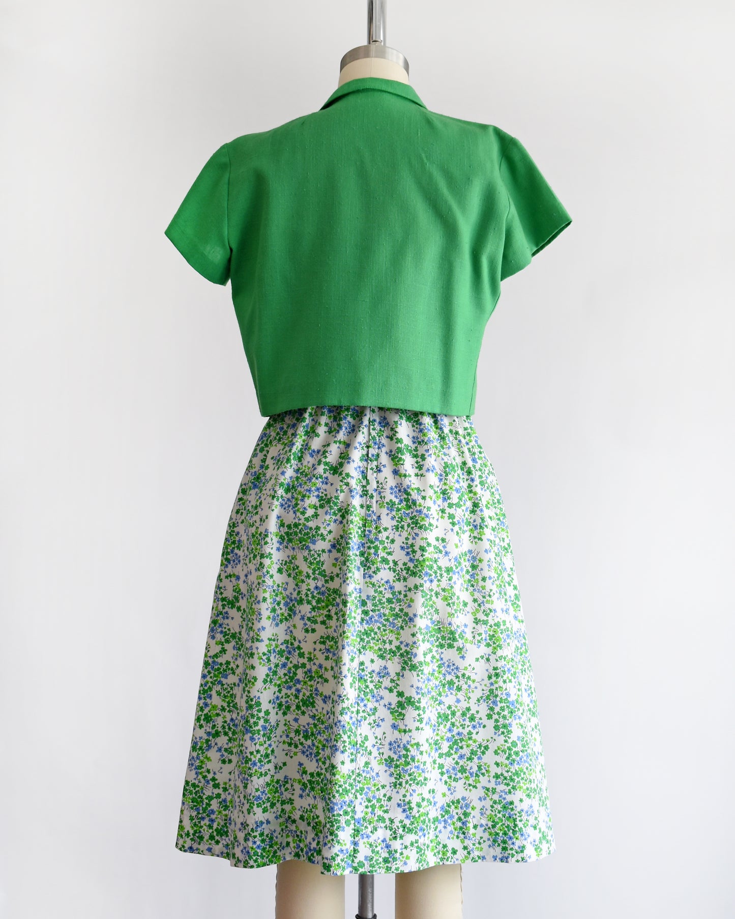 back view of side by side side views of a vintage 1970s green floral dress with green bolero on a mannequin against a white background.
