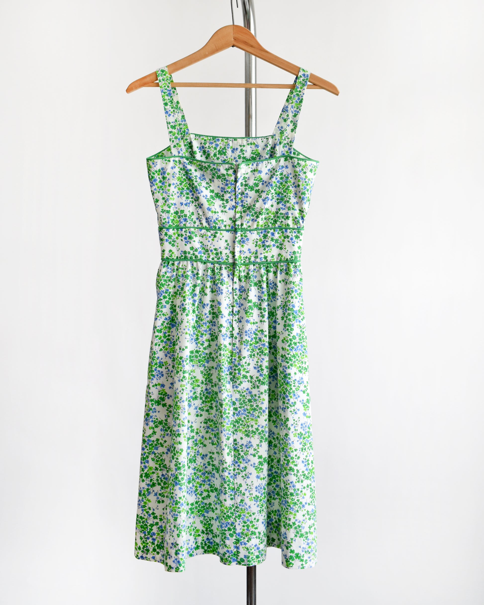 back view of a vintage 1970s green floral dress  on a hanger against a white background.