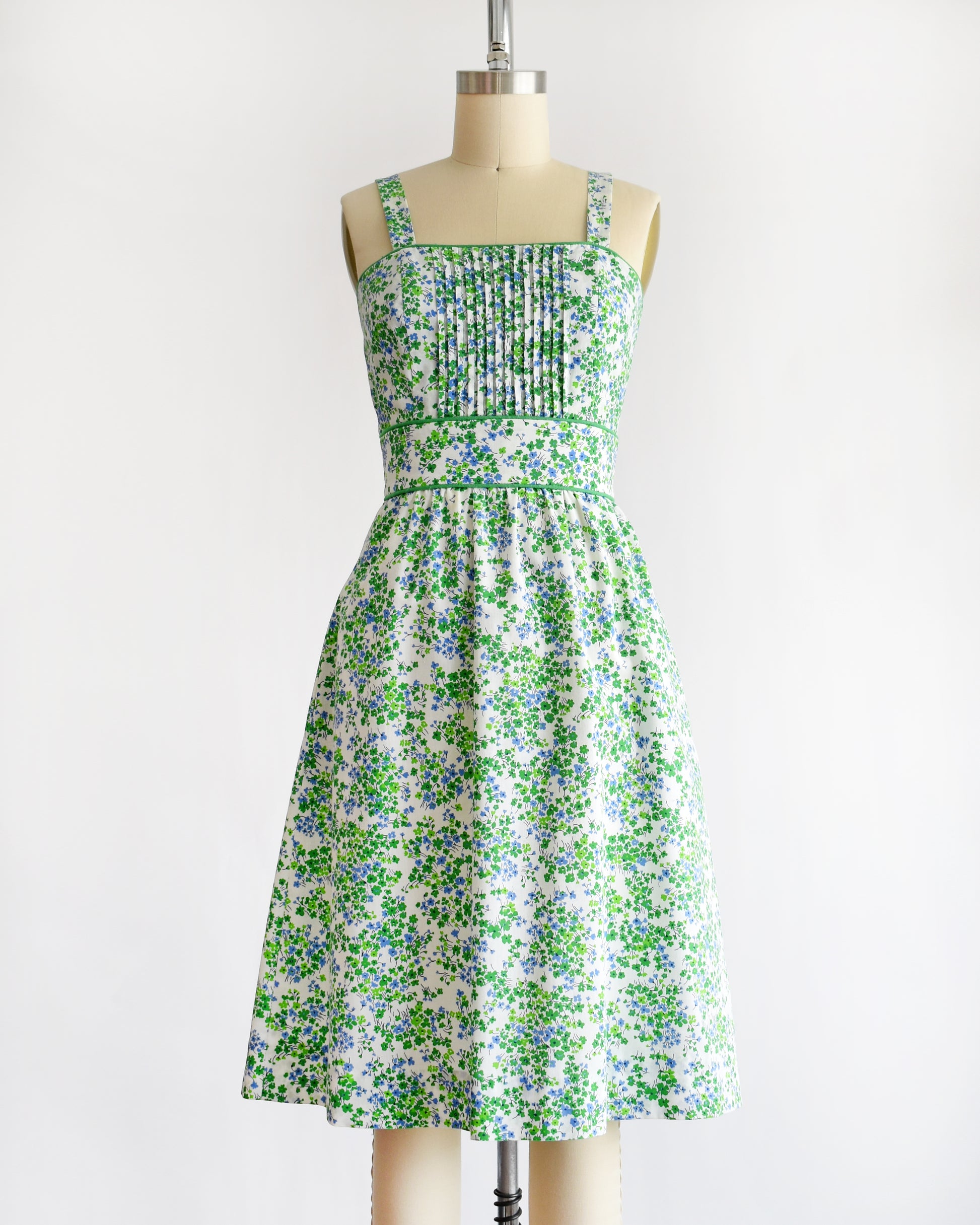 a vintage 1970s green and blue floral dress set on a mannequin against a white background