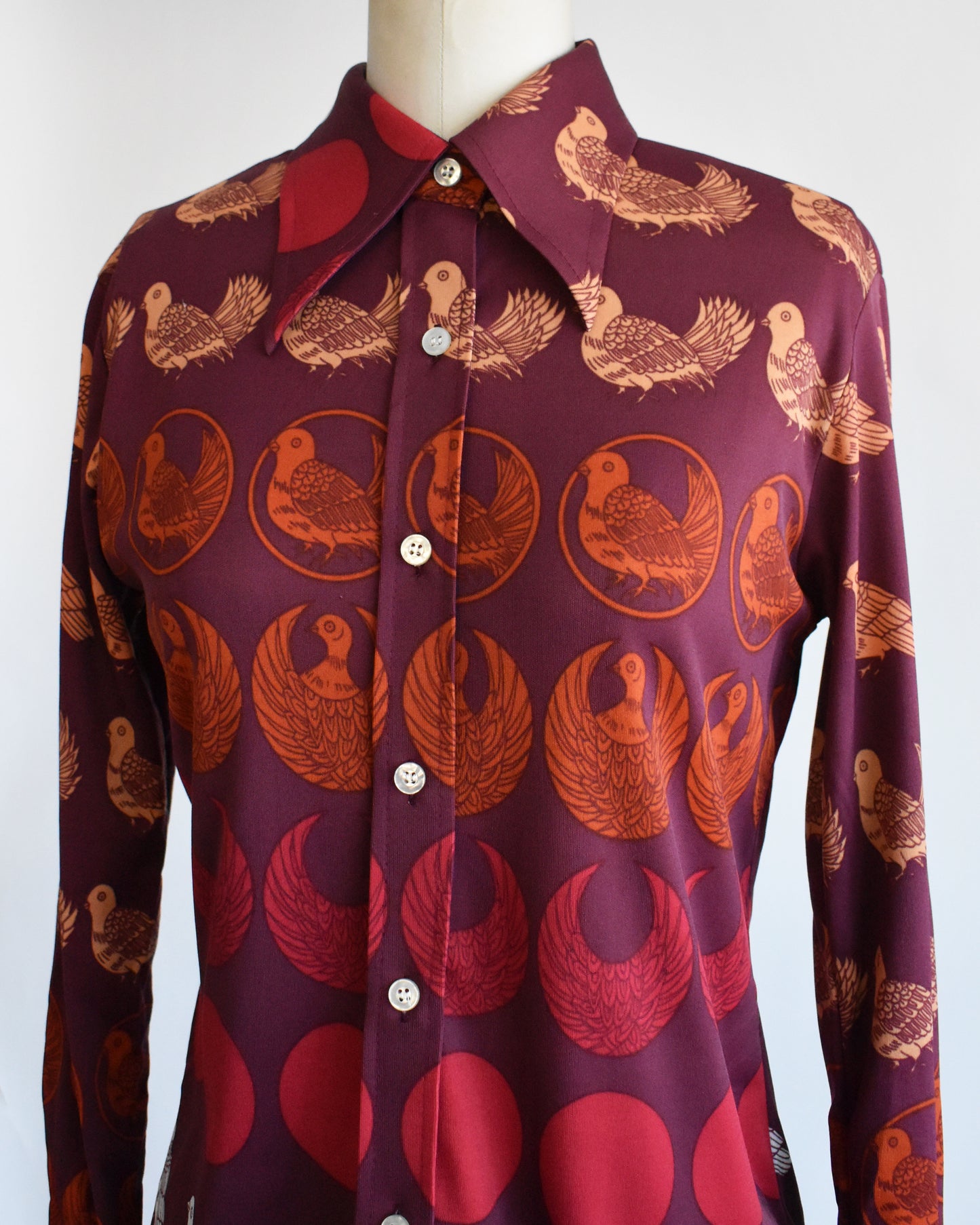 close up of a vintage 1970s red patterned bird shirt on a mannequin against a white background