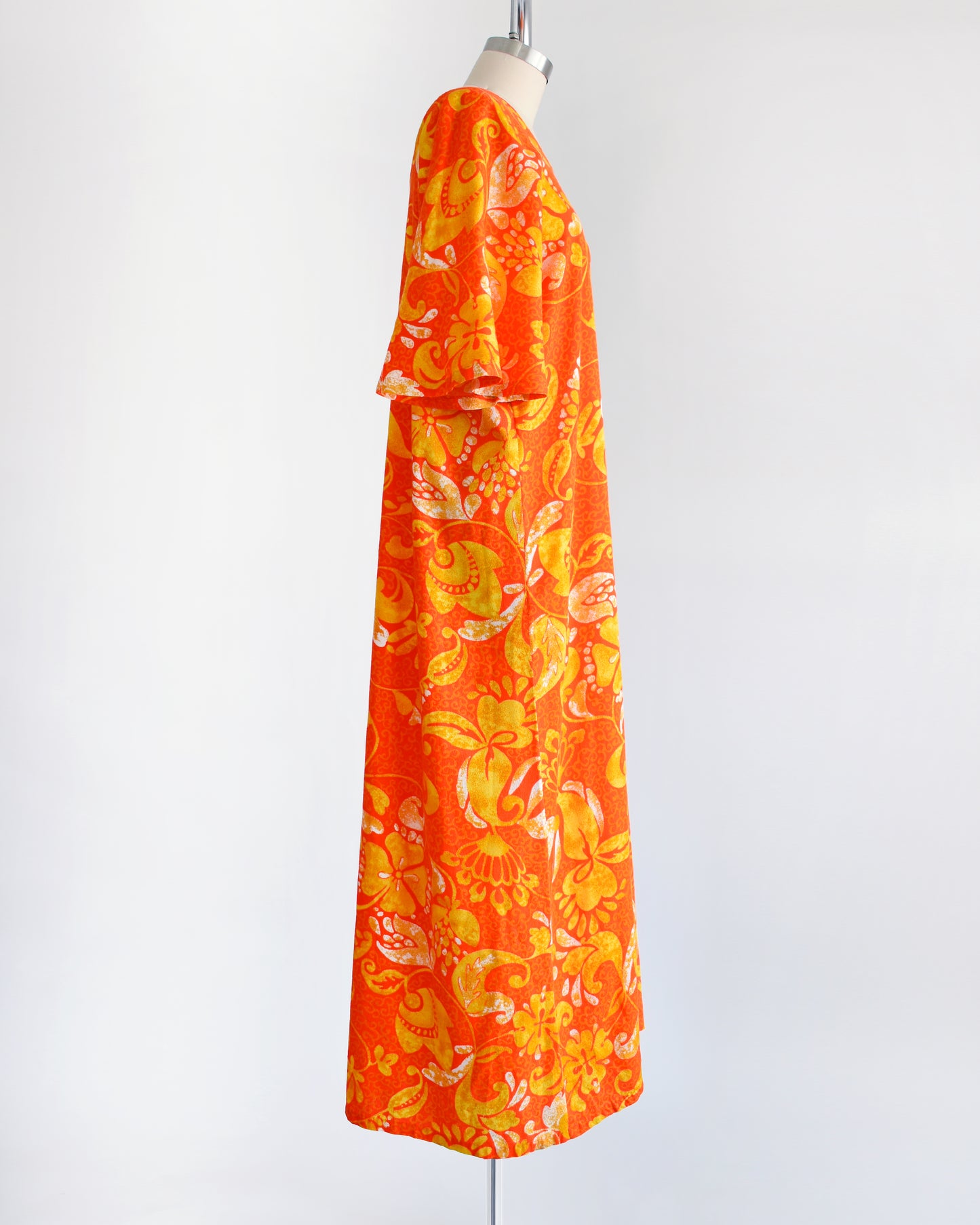 side view of a vintage 1970s orange floral maxi caftan dress on a mannequin against a white background