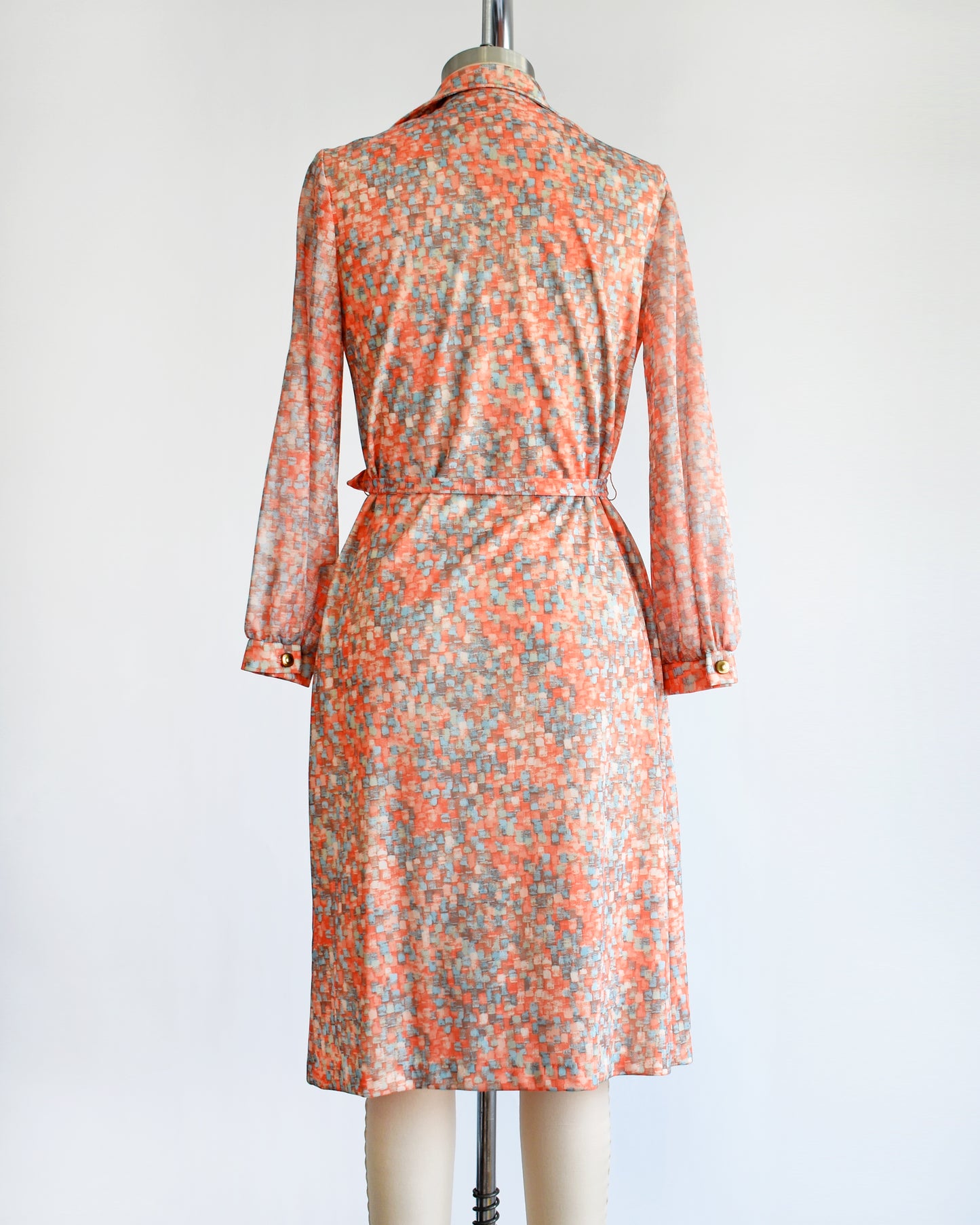 back view of a vintage 1970s orange and blue dress on a mannequin against a white background
