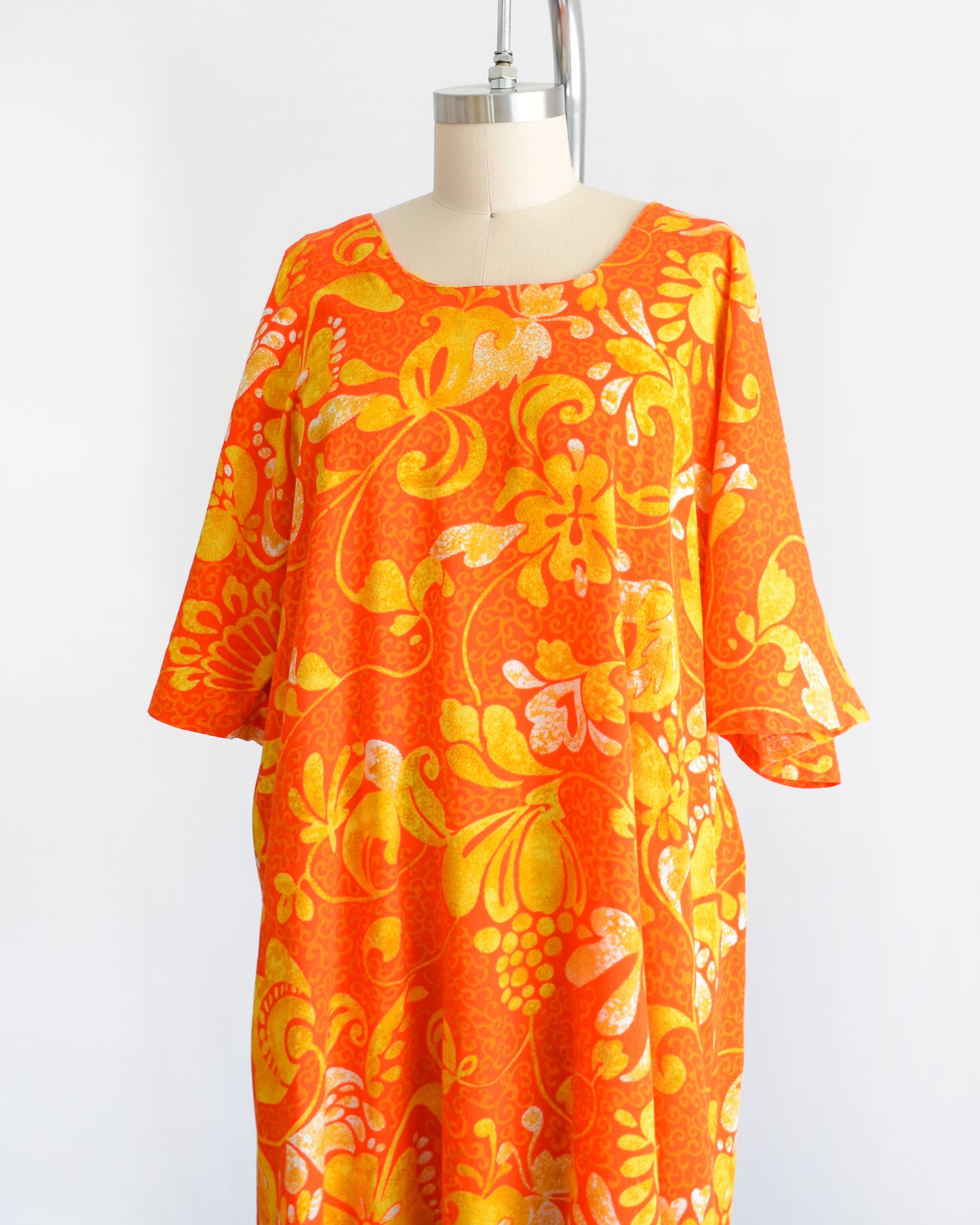 side front view of a vintage 1970s orange floral maxi caftan dress on a mannequin against a white background