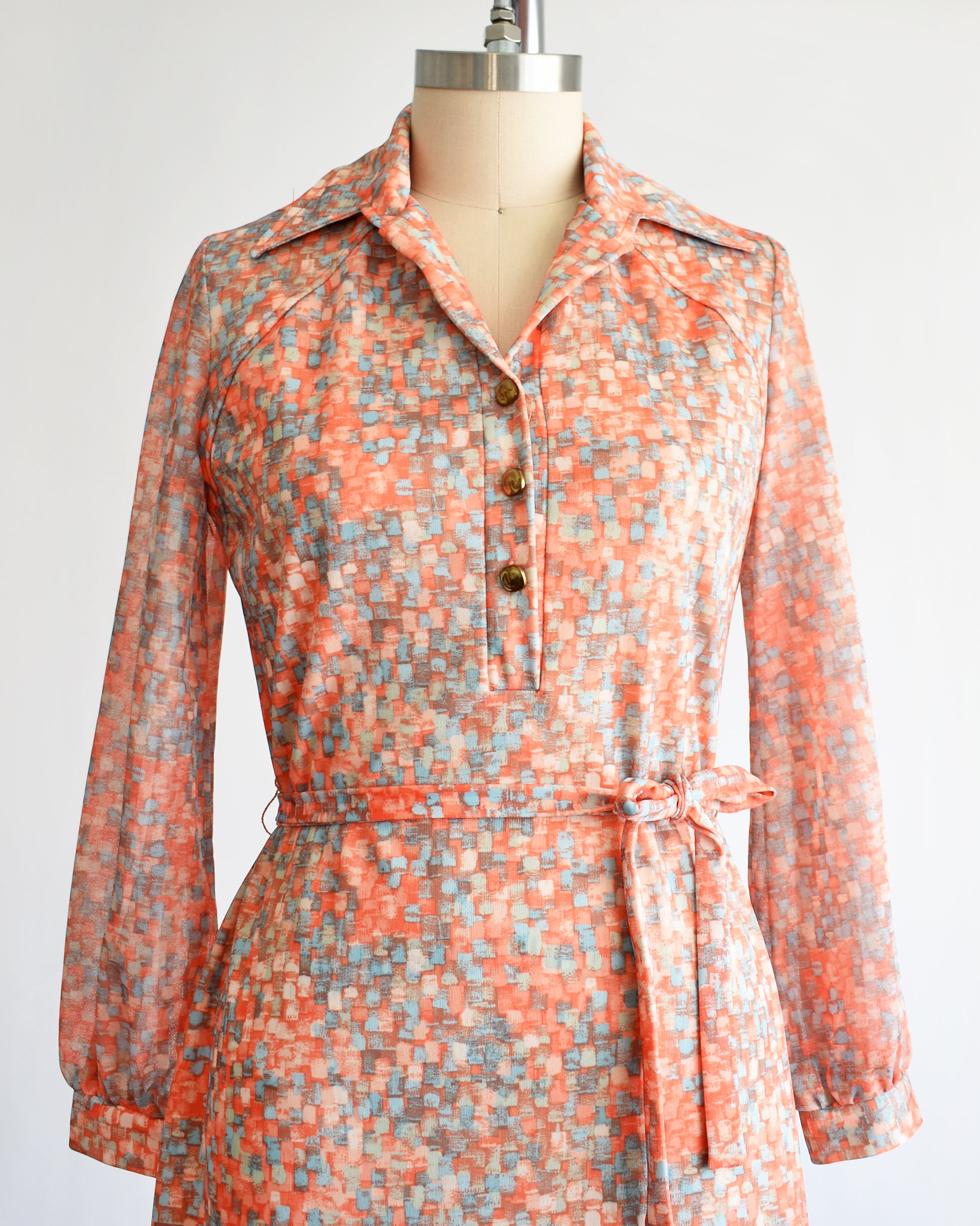 close up of the bodice on a vintage 1970s orange and blue dress on a mannequin against a white background