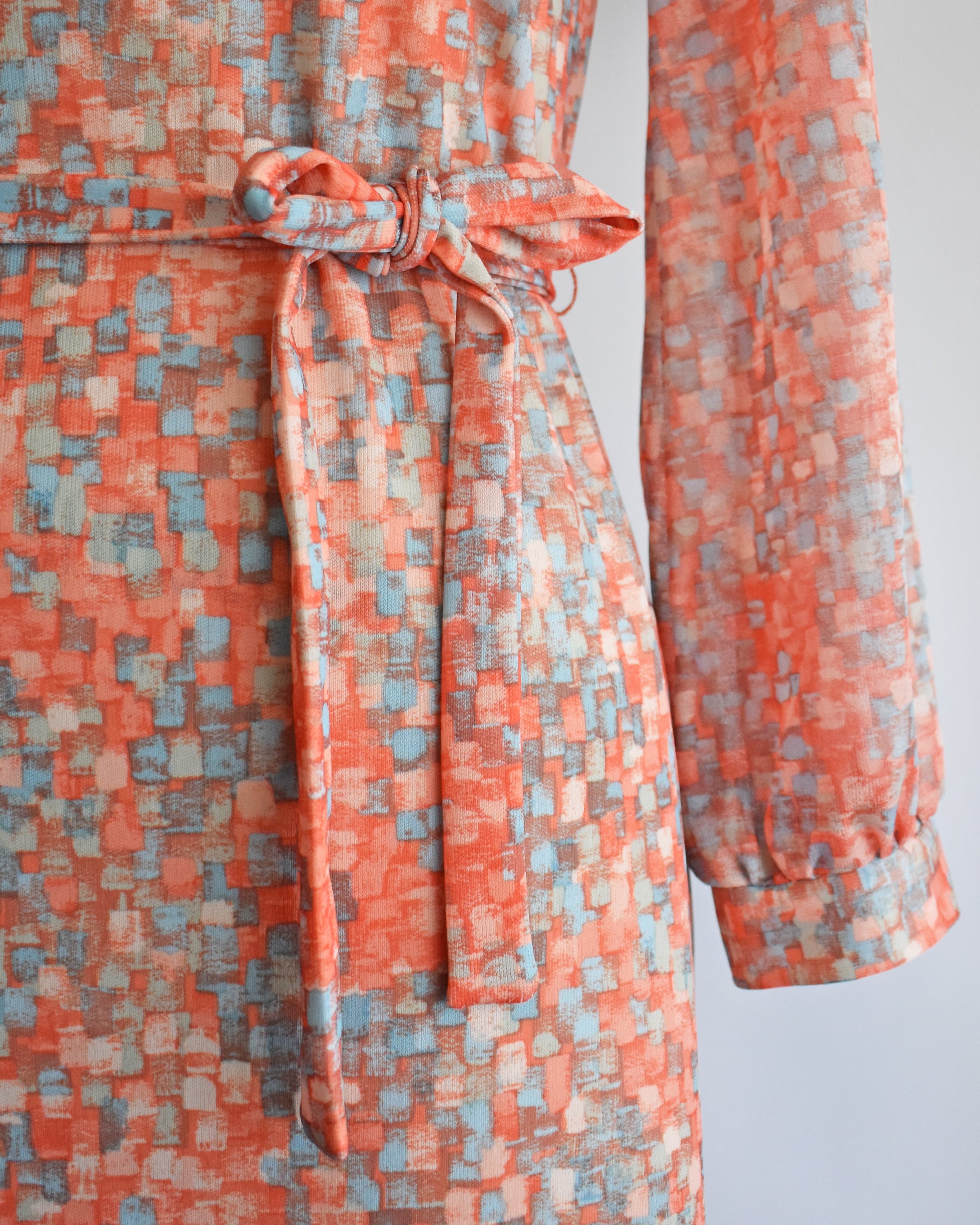 close up of the waist and belt on a vintage 1970s orange and blue dress on a mannequin against a white background