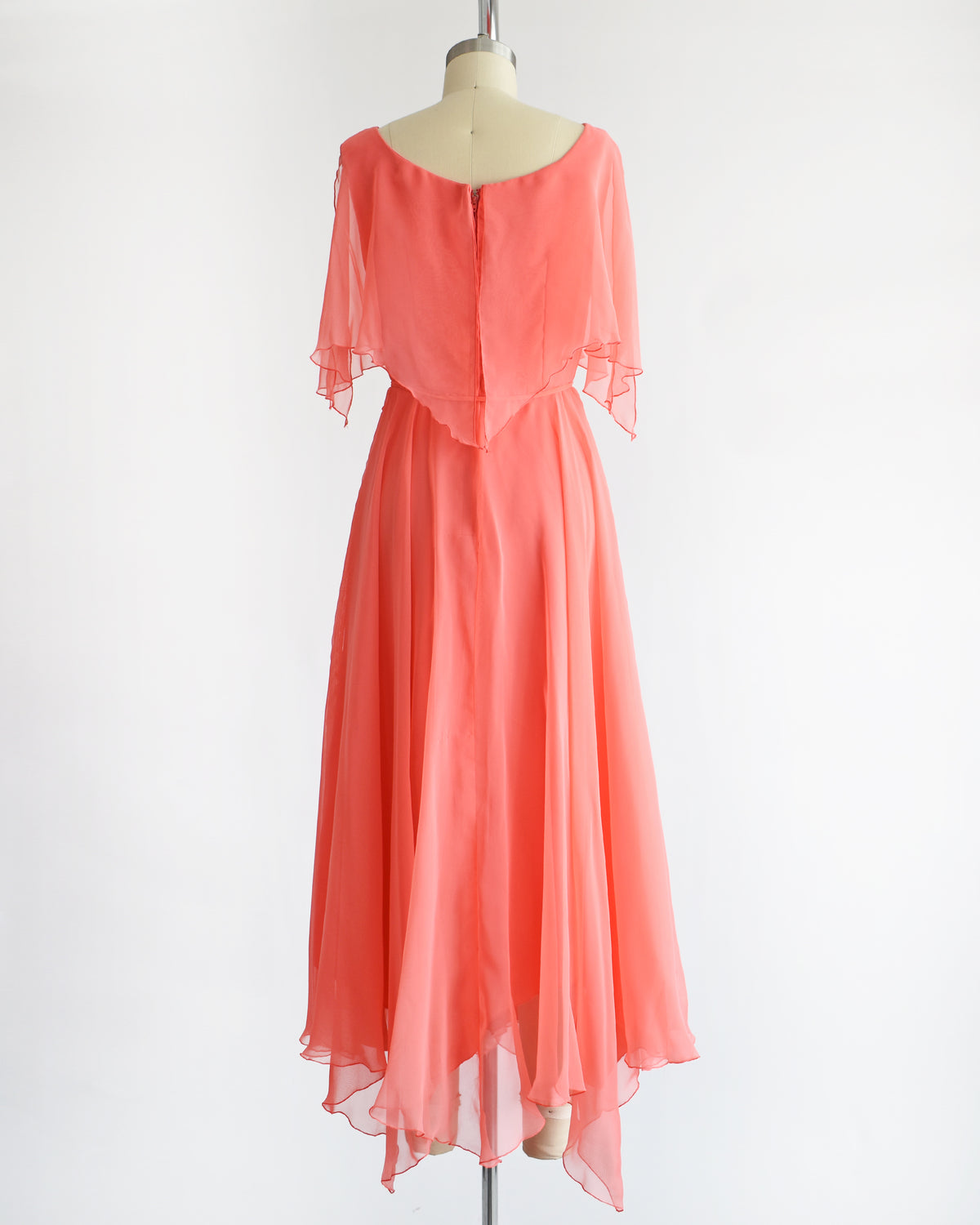 back view of a vintage 1970s coral flutter dress on a mannequin against a white background