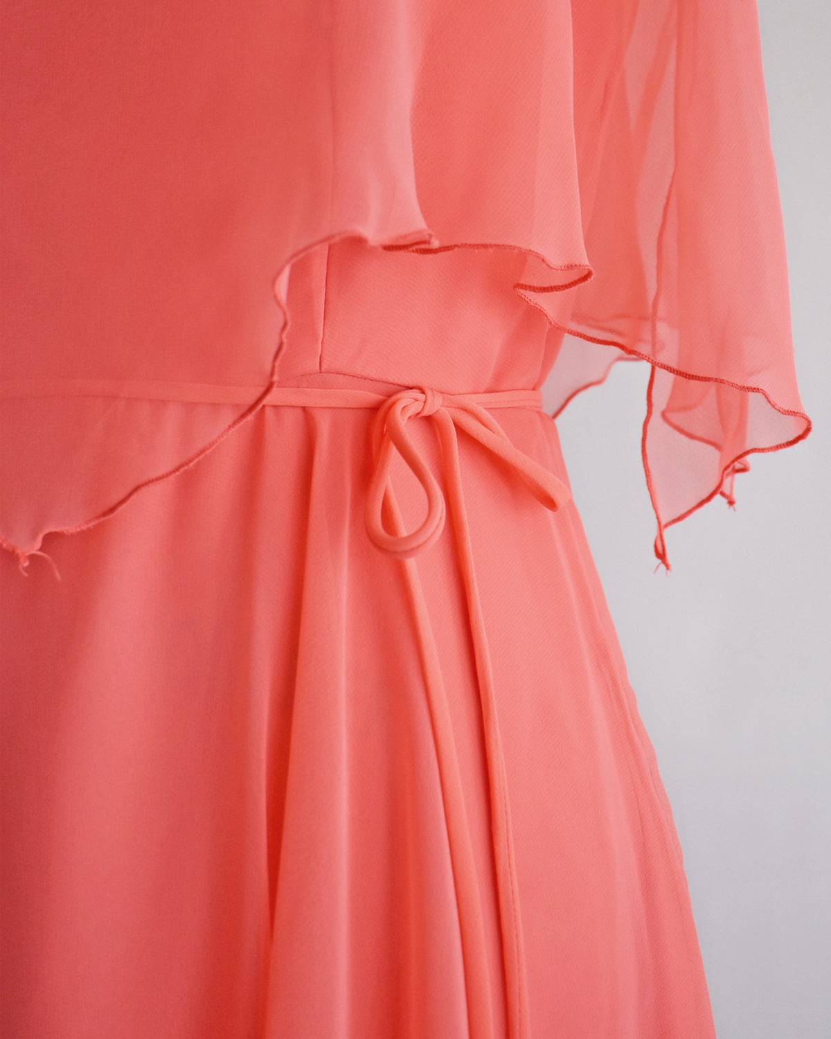 close up of the tie belt on a vintage 1970s coral flutter dress on a mannequin against a white background