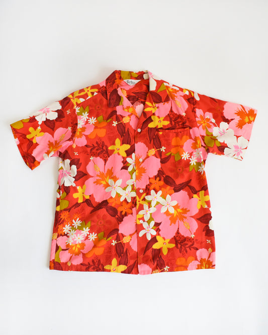 A vintage late 60s early 70s floral Hawaiian shirt. Shades of bright red, pink, orange, yellow, white, and green floral print cover the shirt.