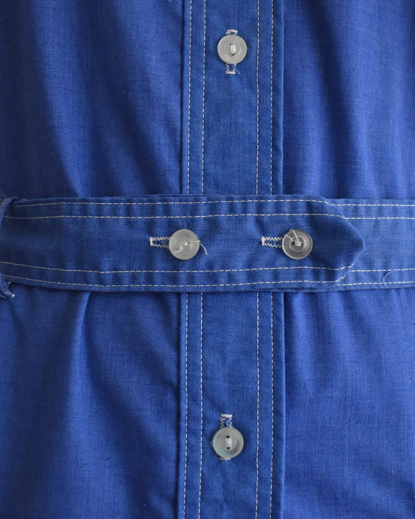 Close-up of the button belt on a vintage 1970s blue dress on a mannequin against a white background