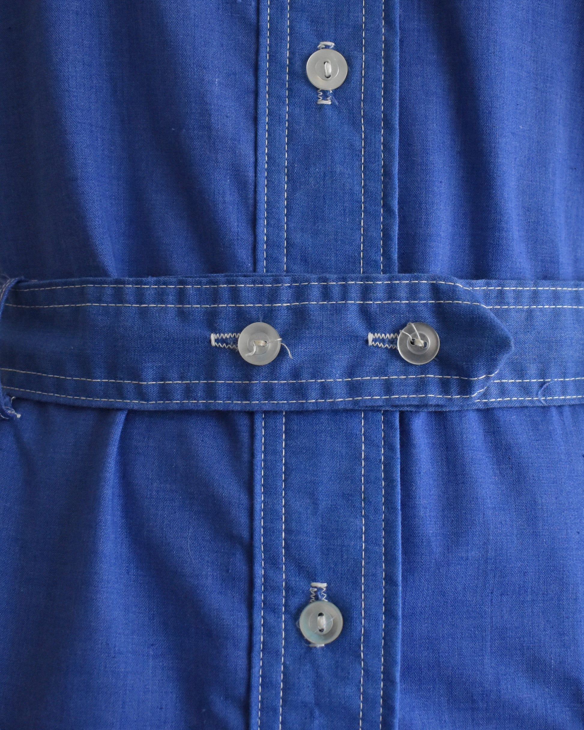 Close-up of the button belt on a vintage 1970s blue dress on a mannequin against a white background