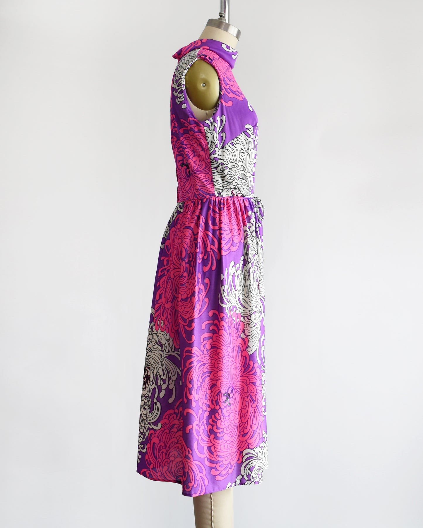 side view of a vintage 1970s purple dress with floral patterns on a mannequin against a white background