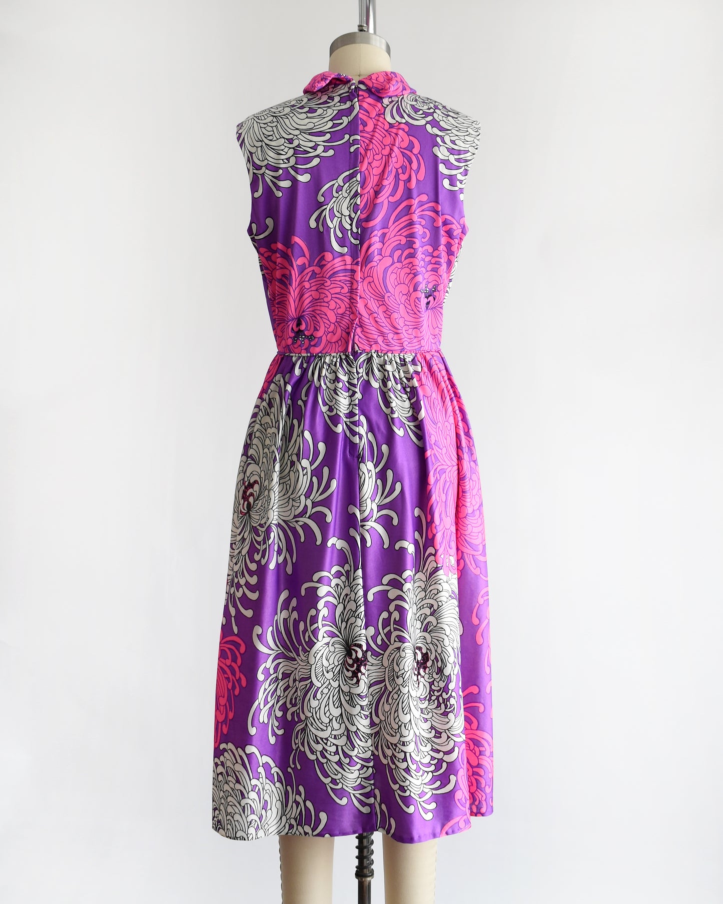back view of a vintage 1970s purple dress with floral patterns on a mannequin against a white background
