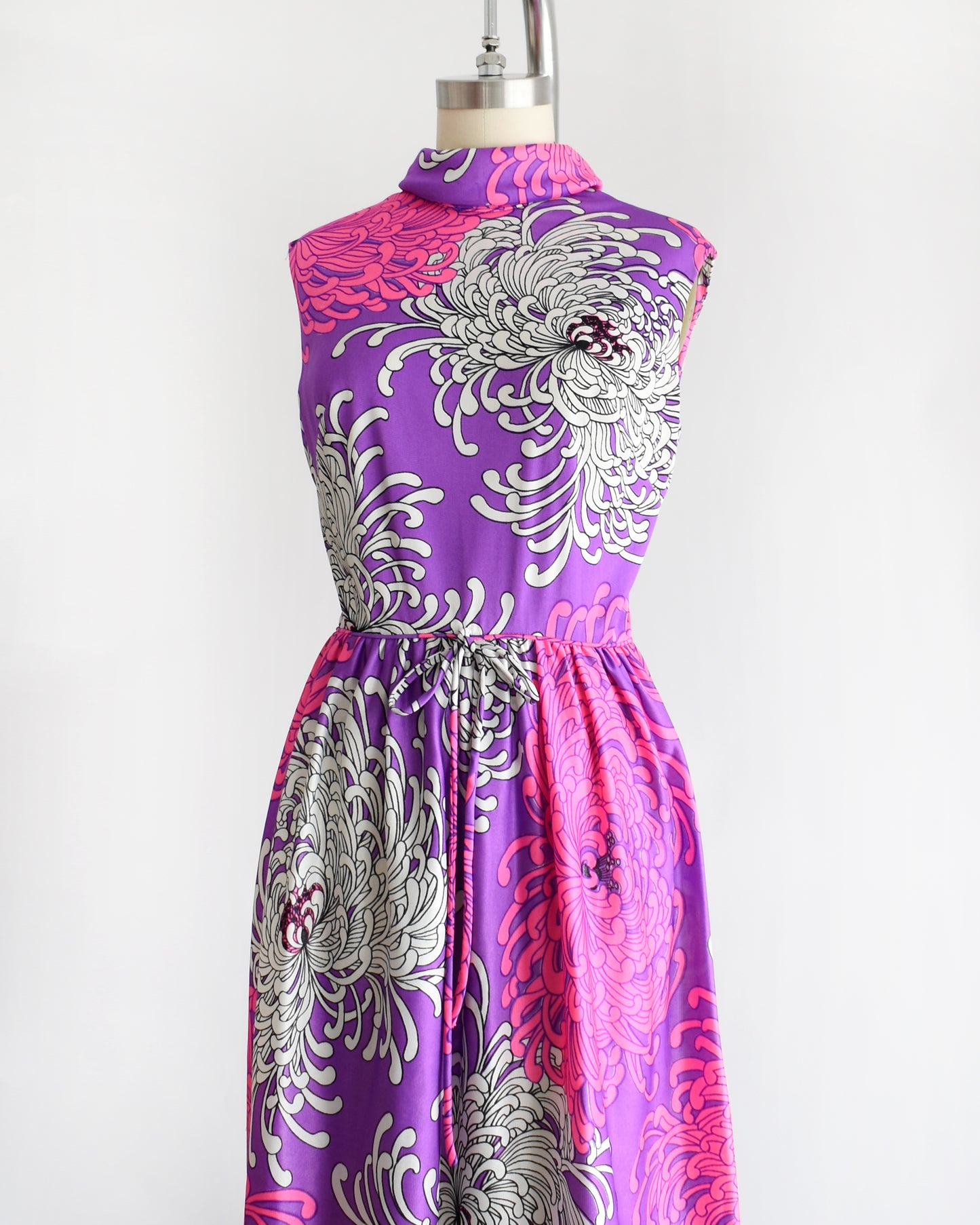 side front view of a vintage 1970s purple dress with floral patterns on a mannequin against a white background