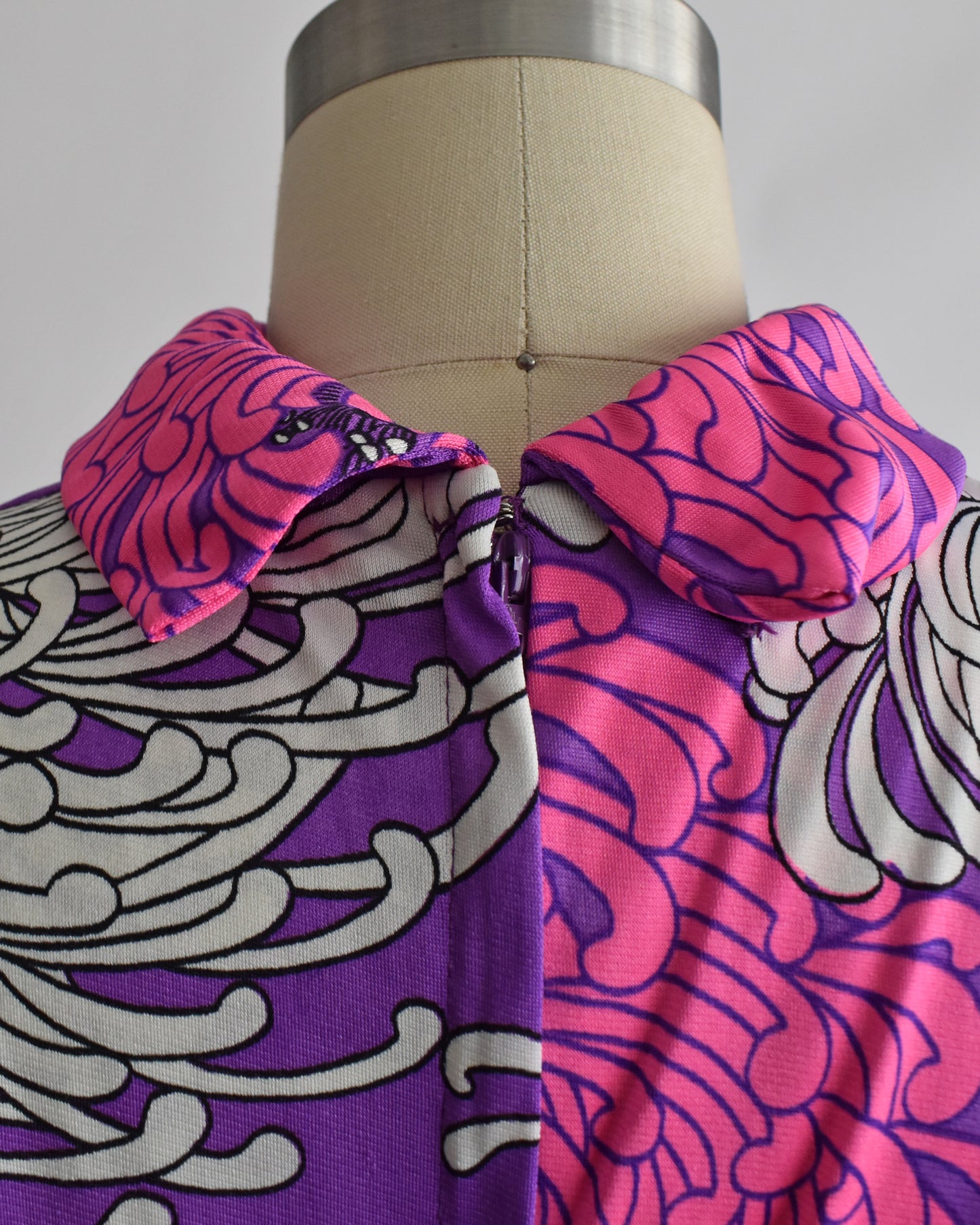 close up of the back of the collar on a vintage 1970s purple dress with floral patterns on a mannequin against a white background