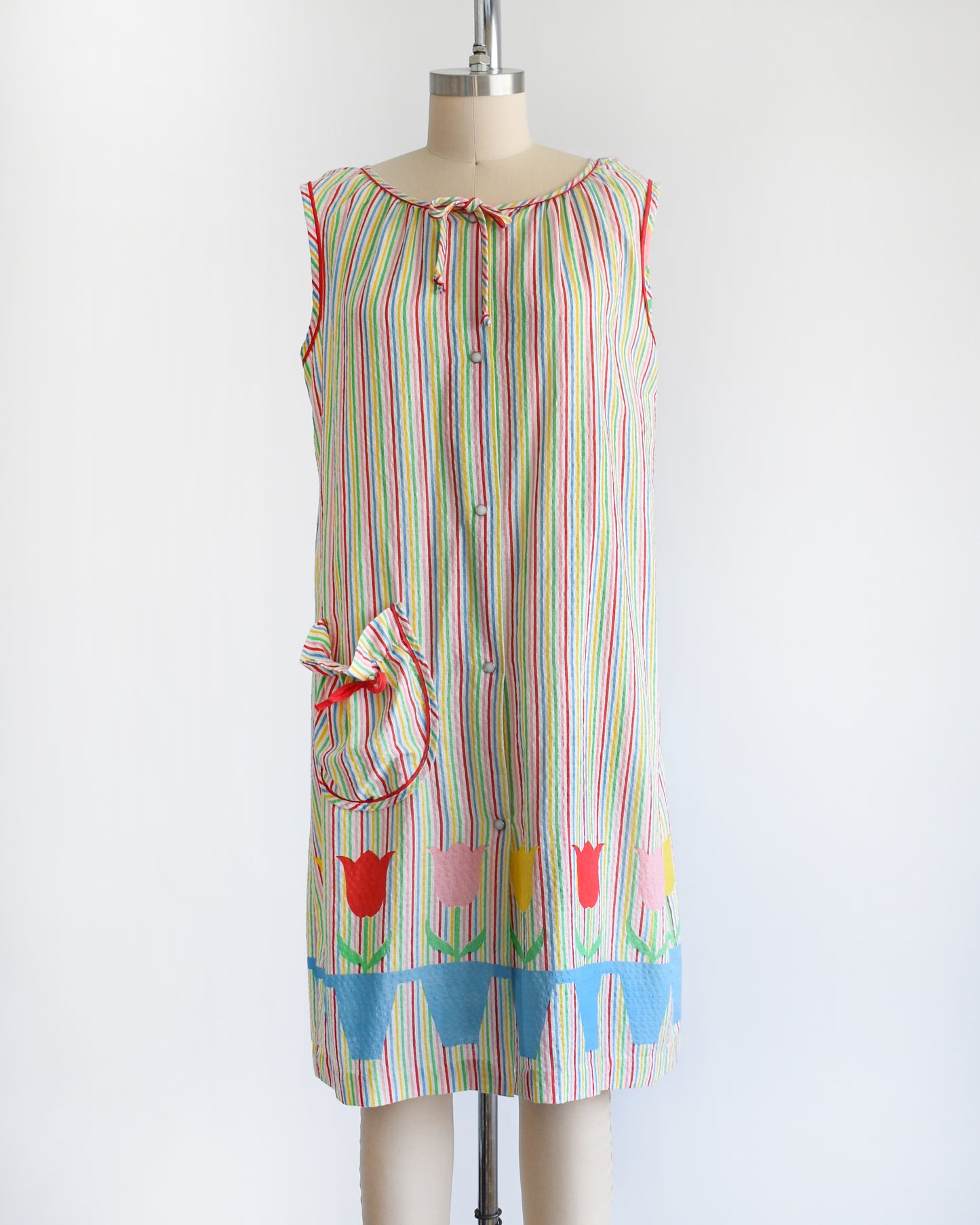 a vintage 1970s rainbow striped house dress with tulips around the hem on a mannequin against a white background