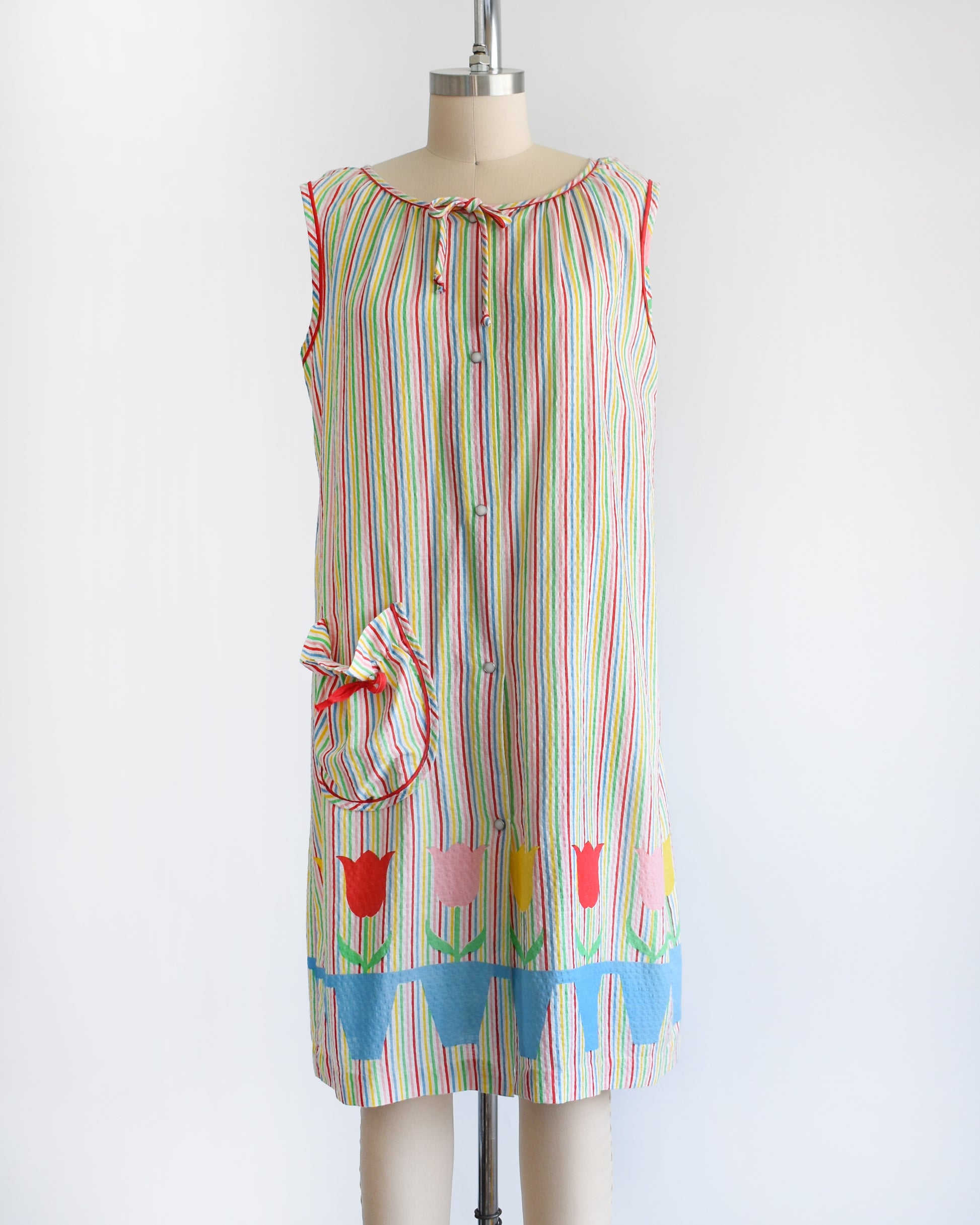 a vintage 1970s rainbow striped house dress with tulips around the hem on a mannequin against a white background