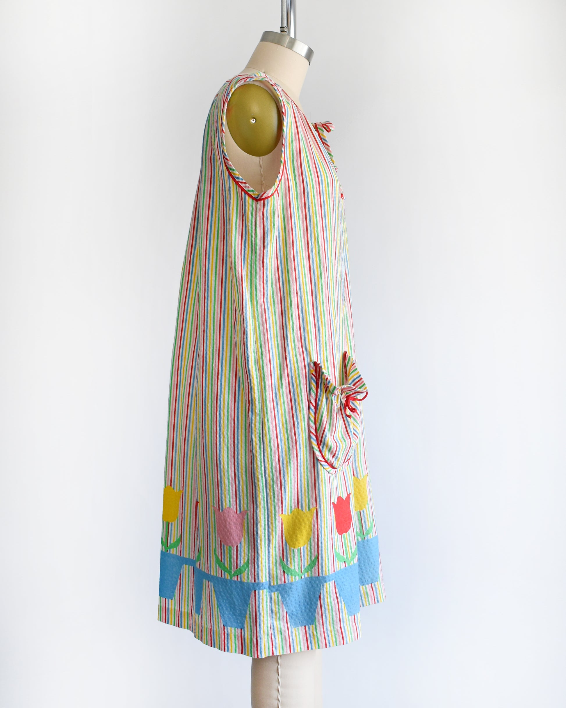 side view of a vintage 1970s rainbow striped house dress with tulips around the hem on a mannequin against a white background