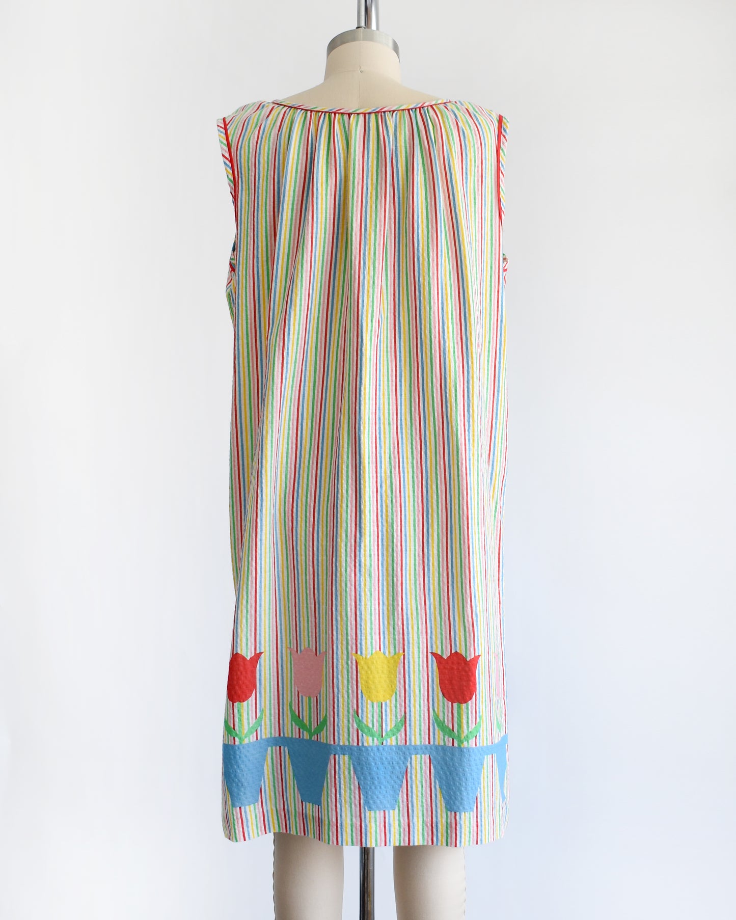 back view of a vintage 1970s rainbow striped house dress with tulips around the hem on a mannequin against a white background