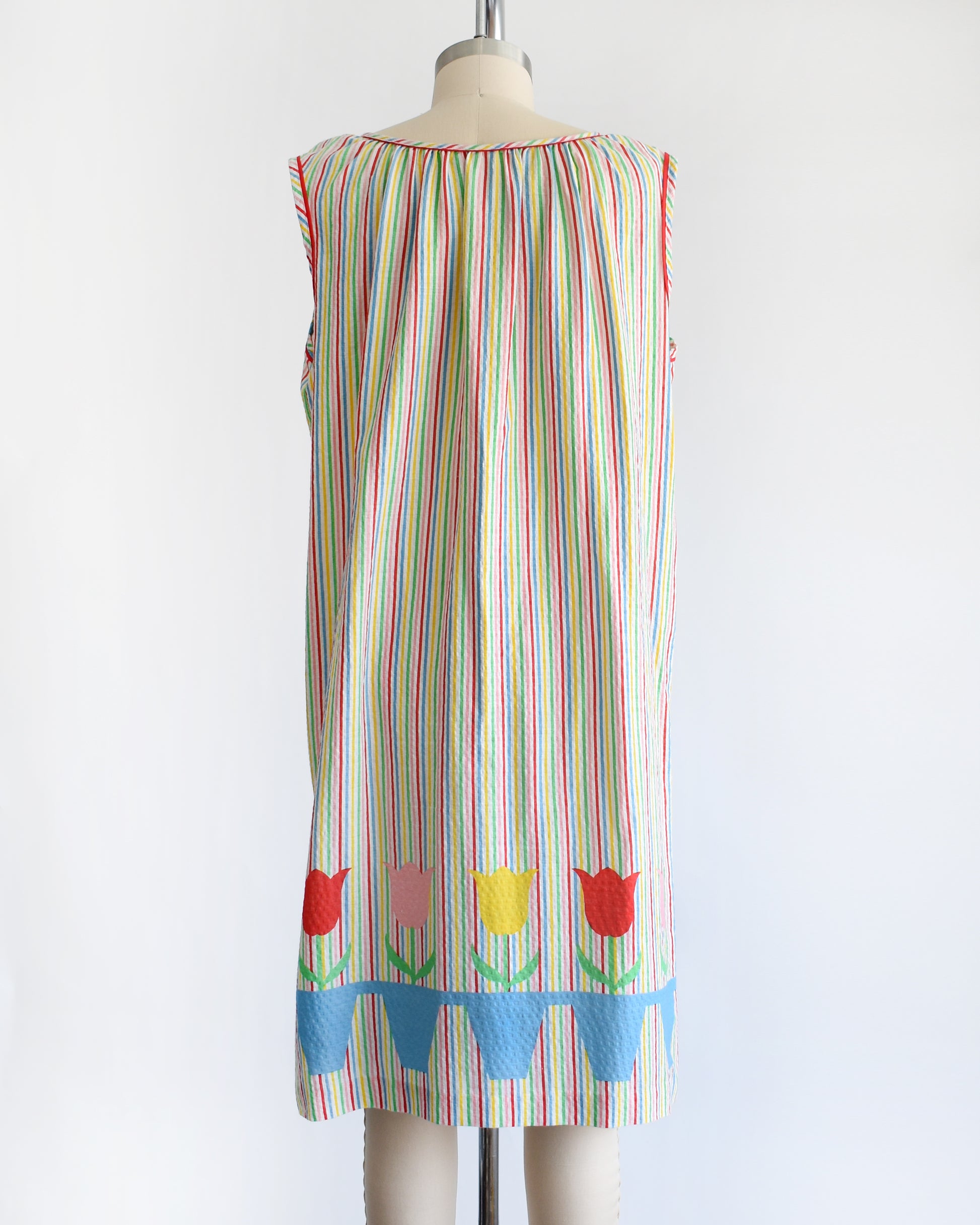 back view of a vintage 1970s rainbow striped house dress with tulips around the hem on a mannequin against a white background
