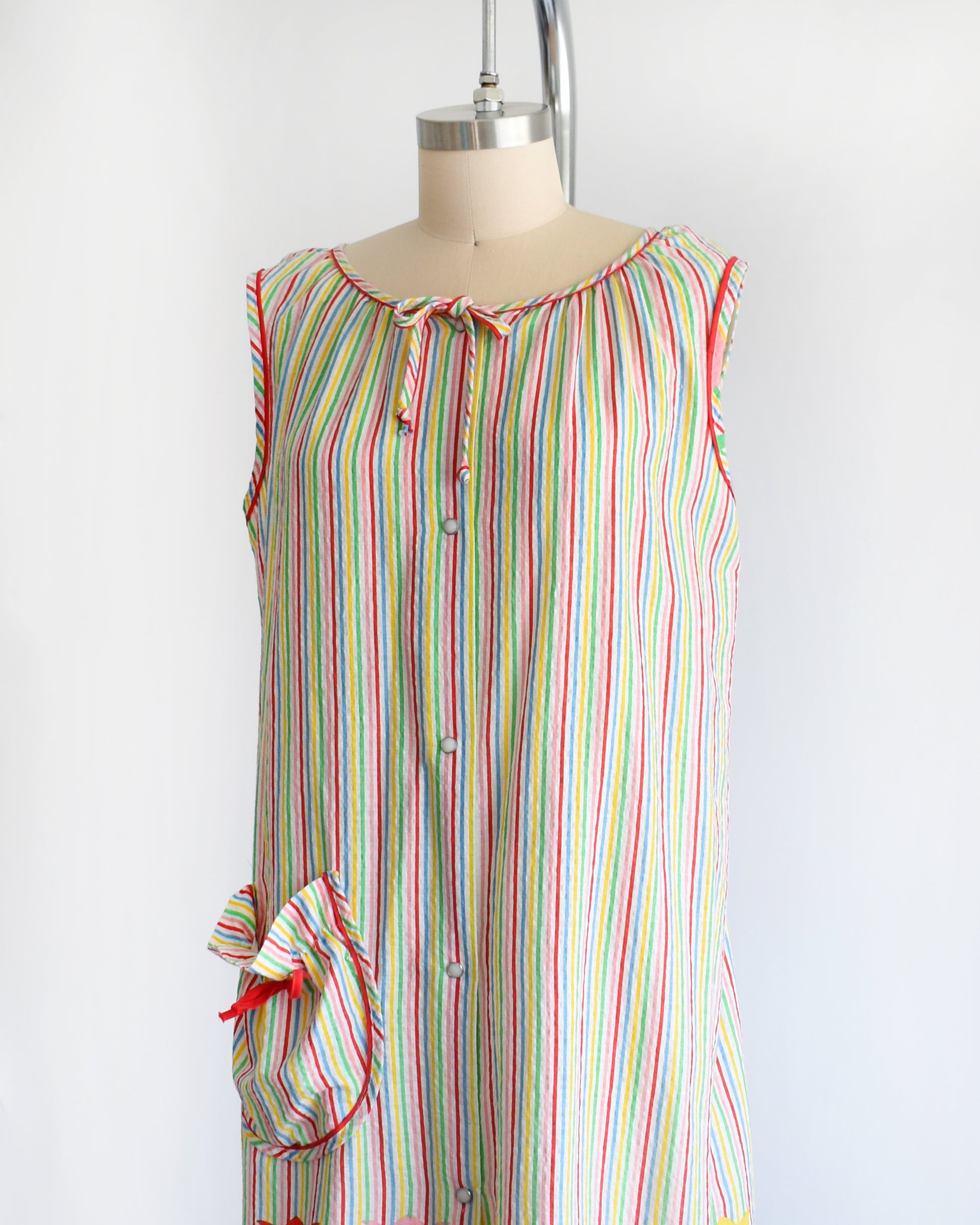 side front view of a vintage 1970s rainbow striped house dress with tulips around the hem on a mannequin against a white background