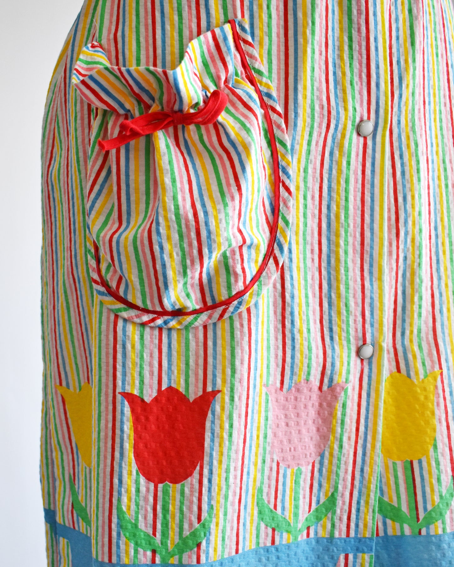close up of the pocket on a vintage 1970s rainbow striped house dress with tulips around the hem on a mannequin against a white background