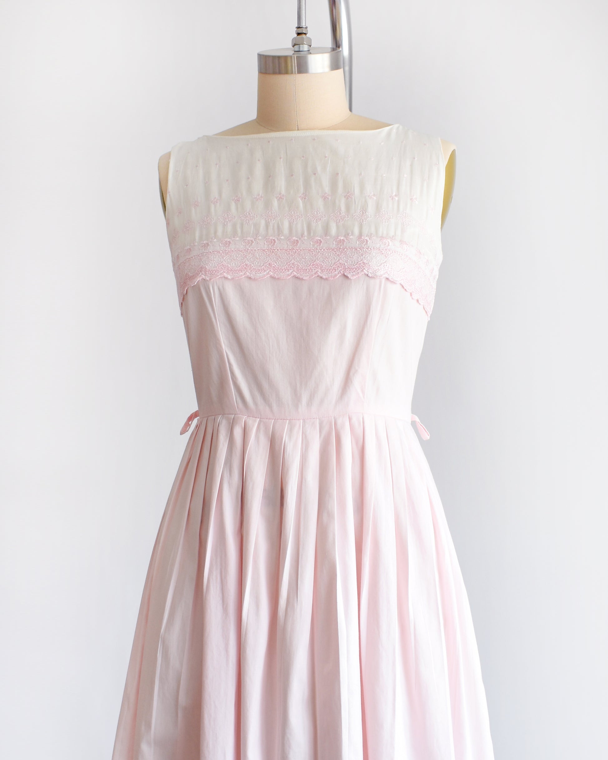 side front view of a vintage 1950s pink and white embroidered dress on a mannequin against a white background