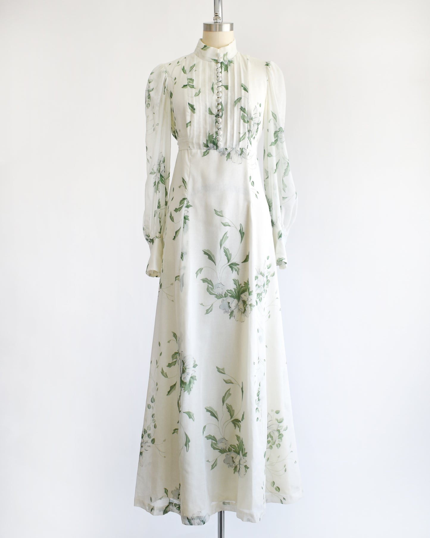 a vintage 1970s white dress with green floral pattern on a mannequin against a white background