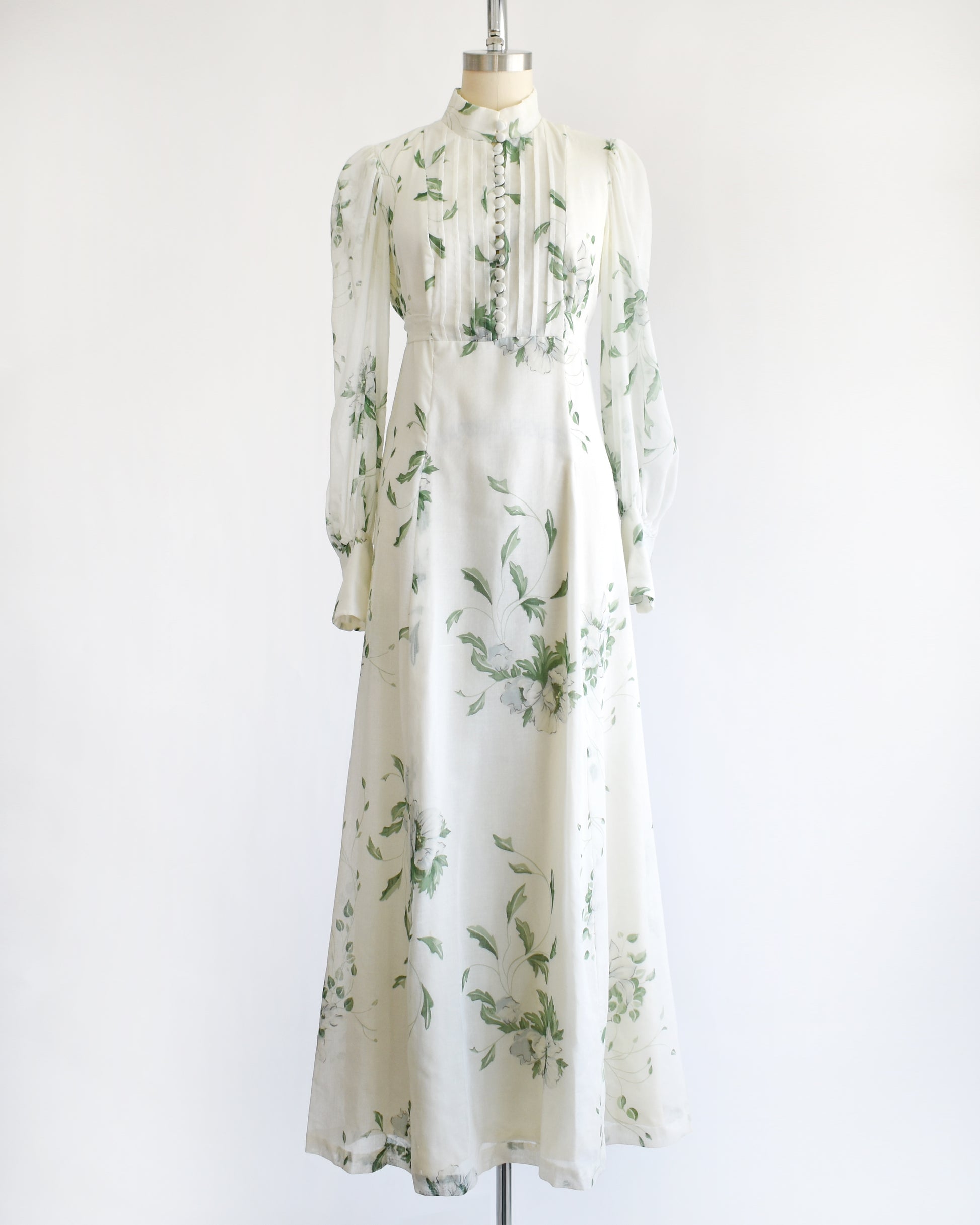a vintage 1970s white dress with green floral pattern on a mannequin against a white background