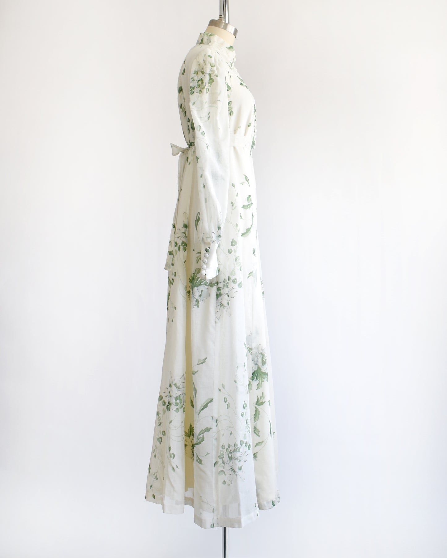 side view of a vintage 1970s white dress with green floral pattern on a mannequin against a white background