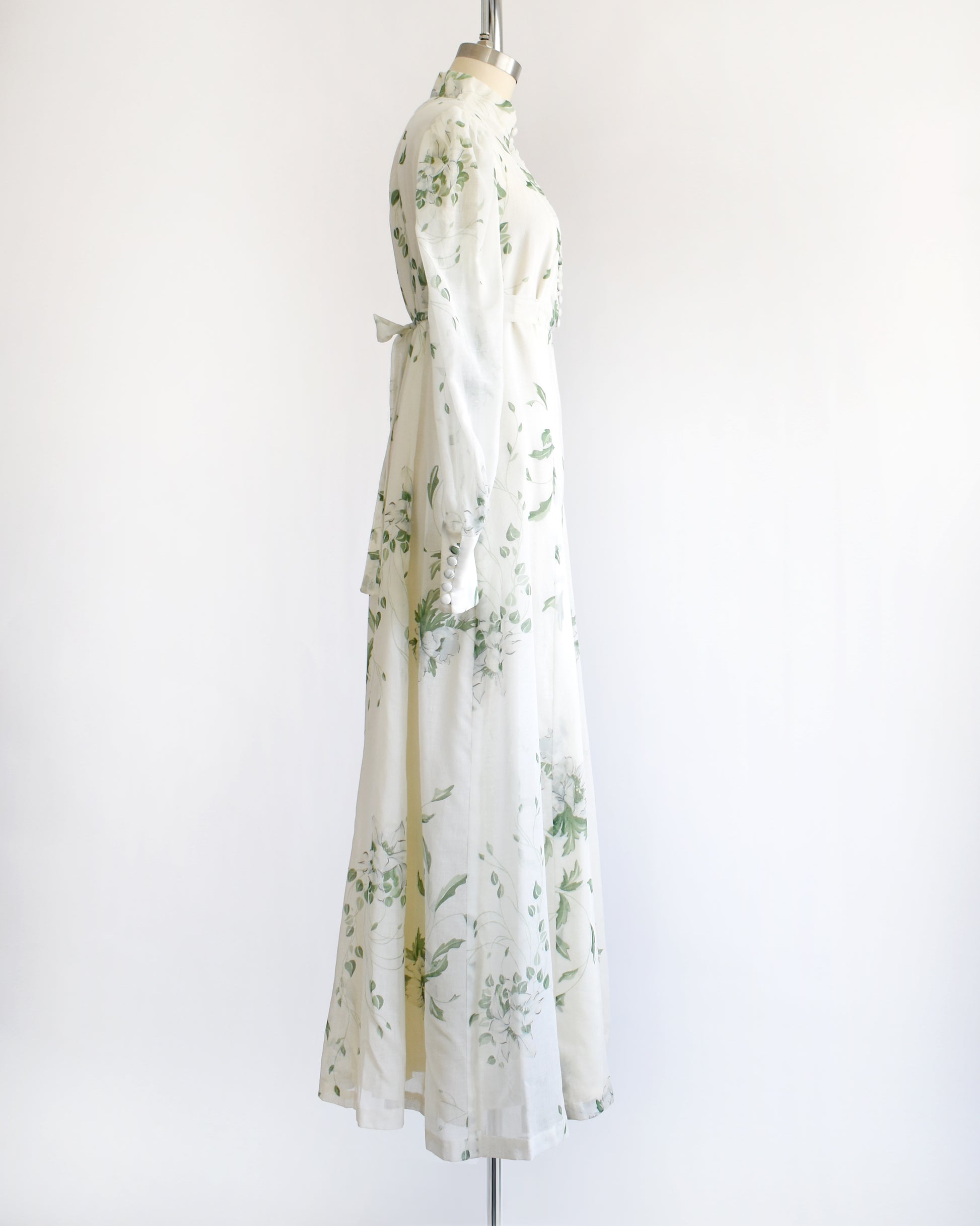 side view of a vintage 1970s white dress with green floral pattern on a mannequin against a white background