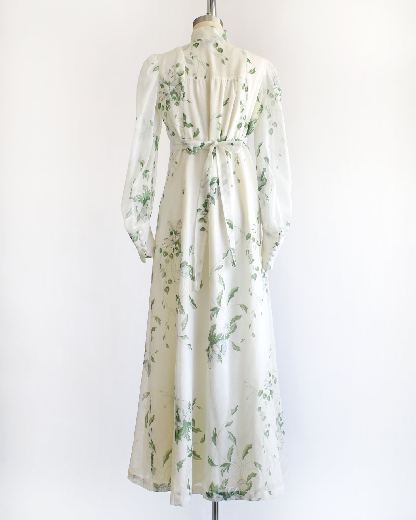 back view of a vintage 1970s white dress with green floral pattern on a mannequin against a white background