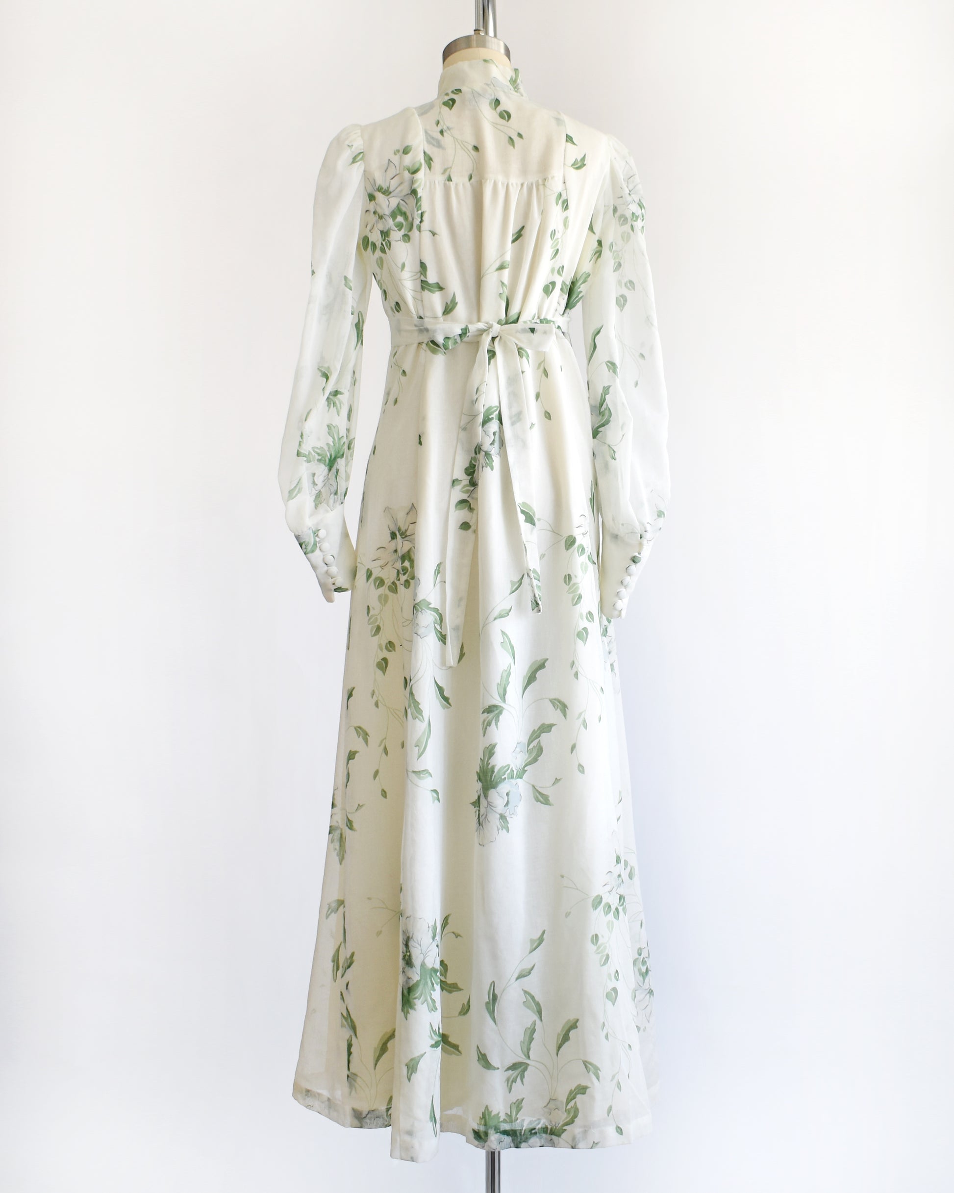 back view of a vintage 1970s white dress with green floral pattern on a mannequin against a white background