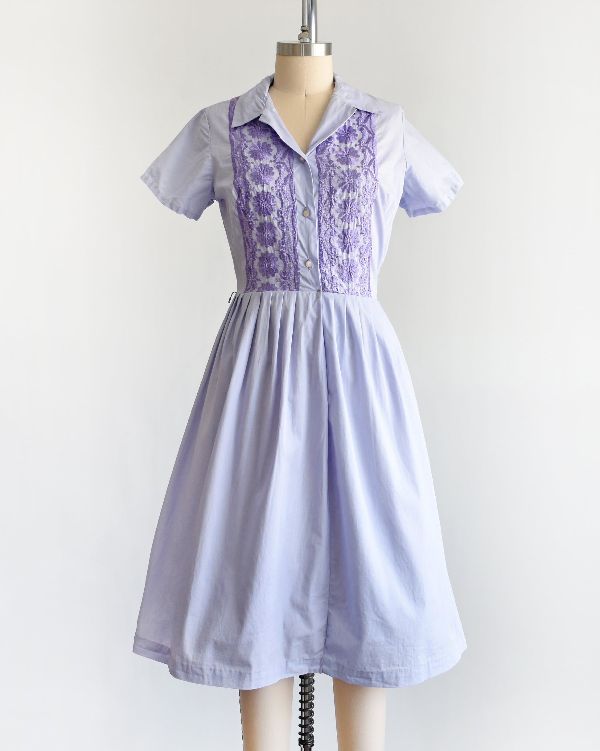 a vintage 1950s light purple dress with dark purple embroidery on a mannequin against a white background