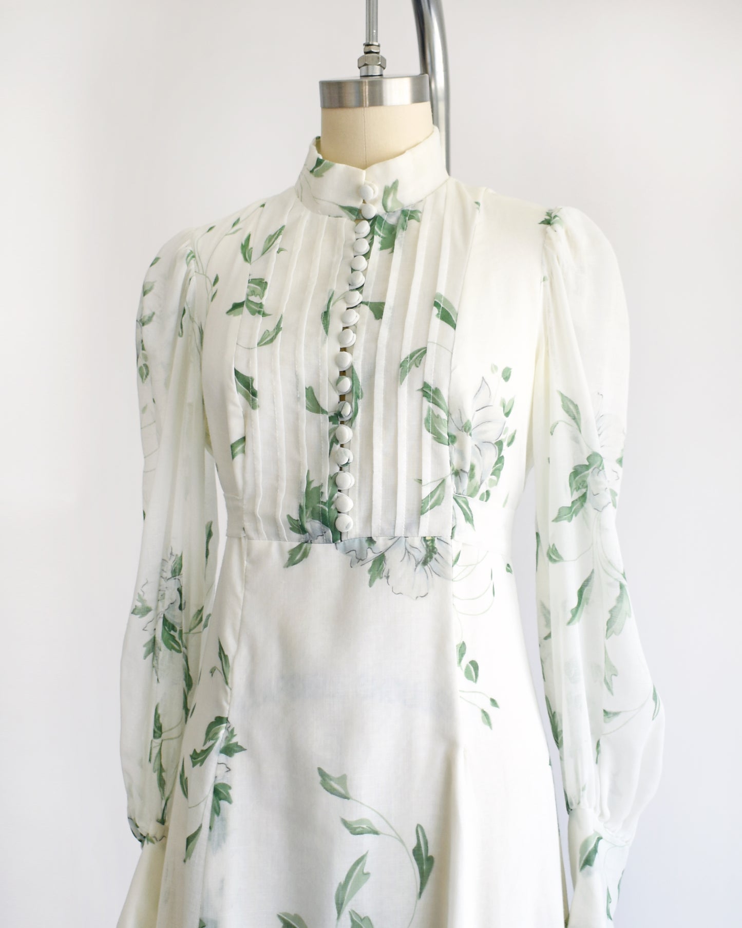 side front view of a vintage 1970s white dress with green floral pattern on a mannequin against a white background