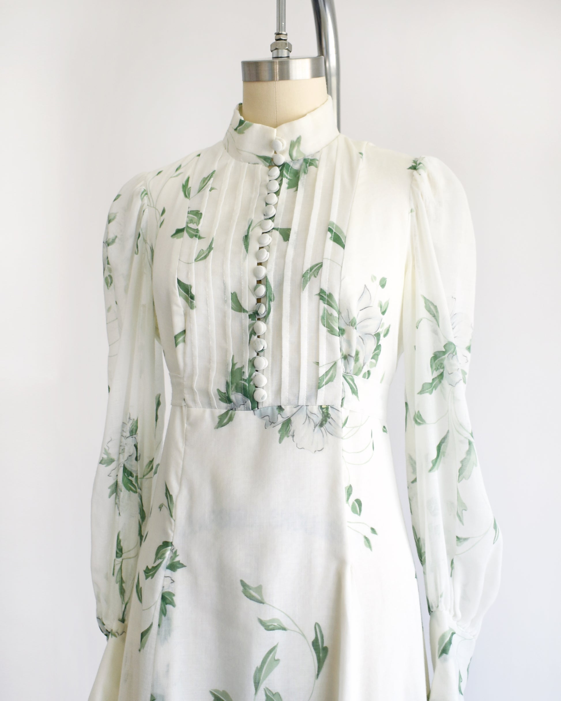 side front view of a vintage 1970s white dress with green floral pattern on a mannequin against a white background