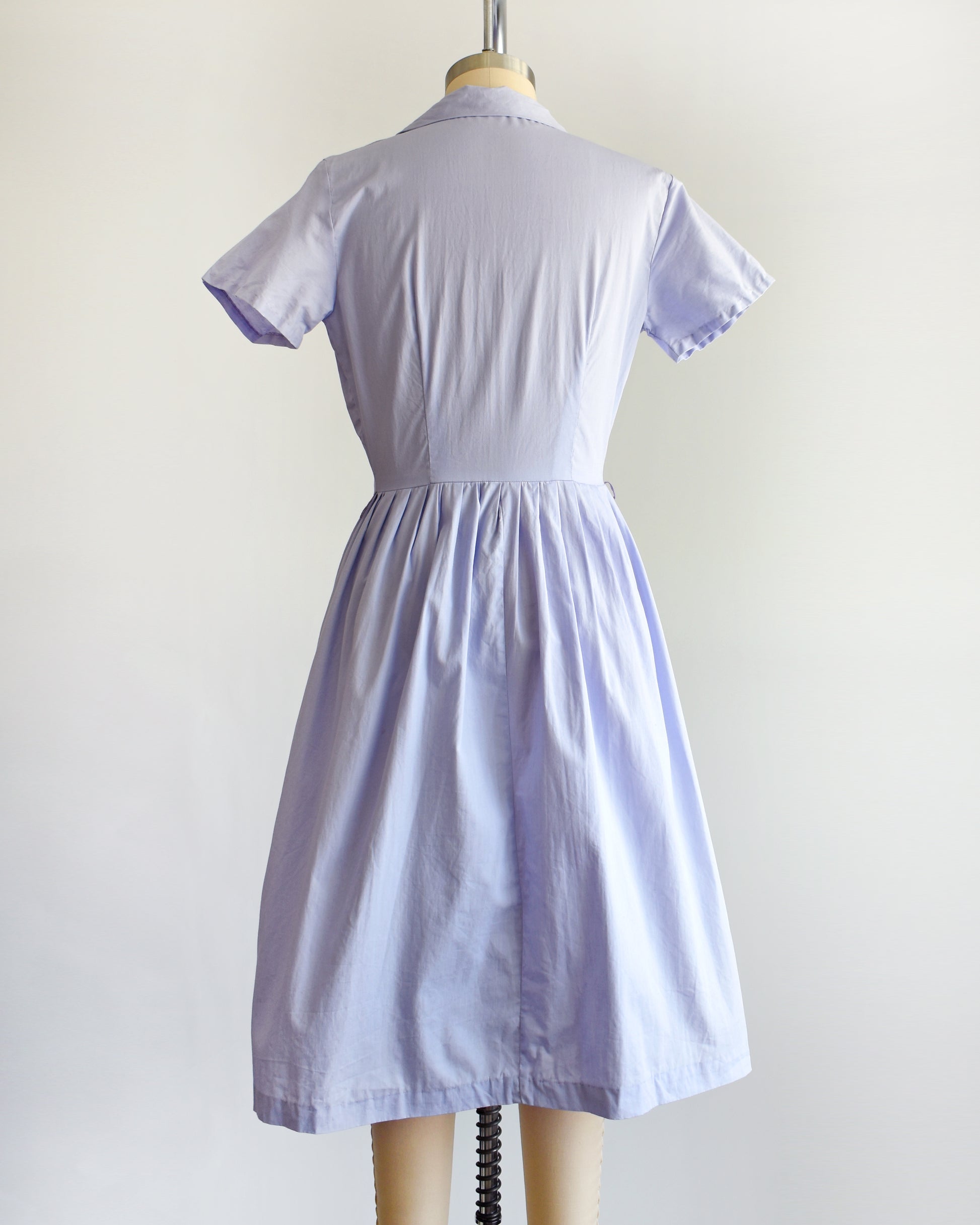back view of a vintage 1950s light purple dress on a mannequin against a white background