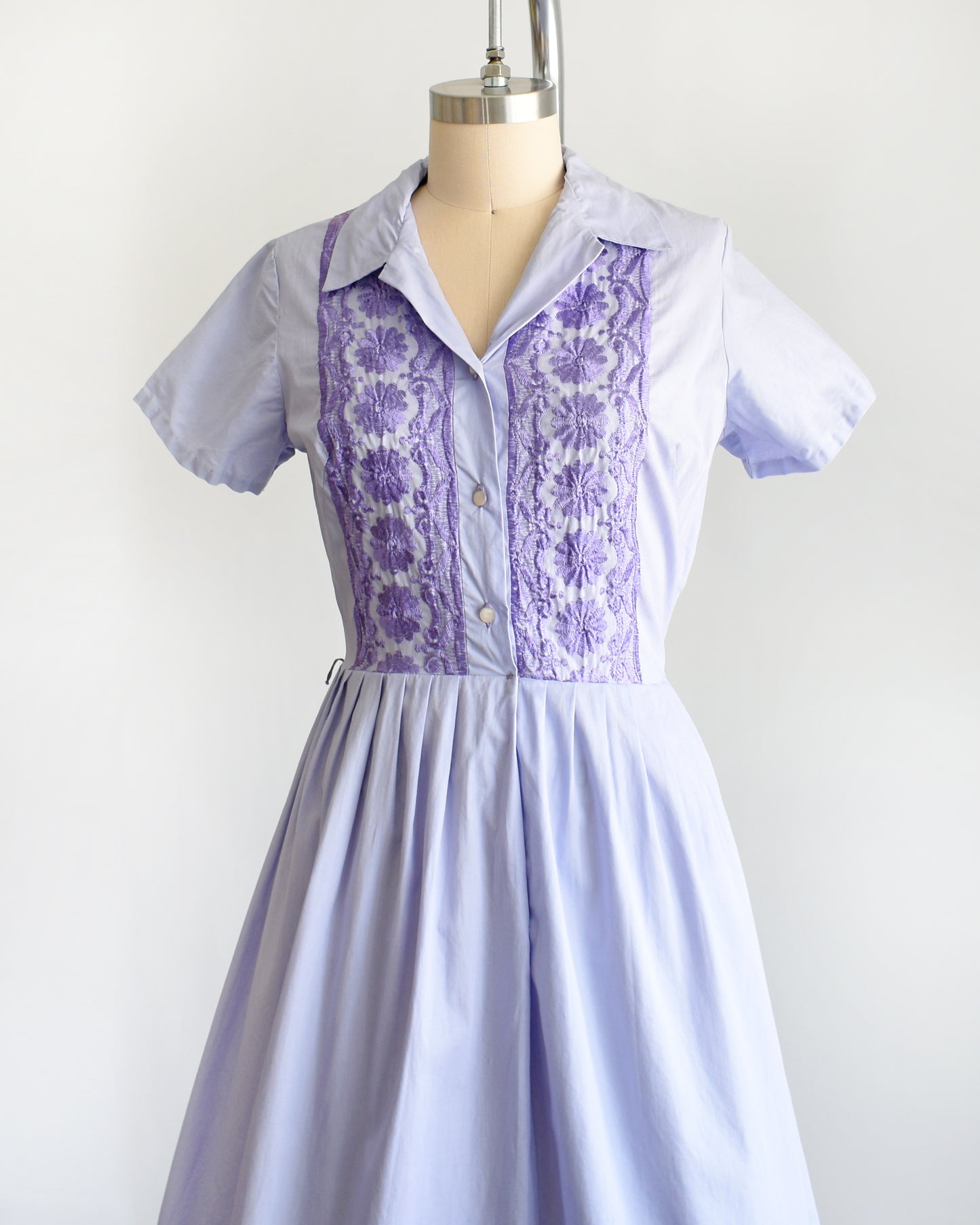 side front view of a vintage 1950s light purple dress with dark purple embroidery on a mannequin against a white background