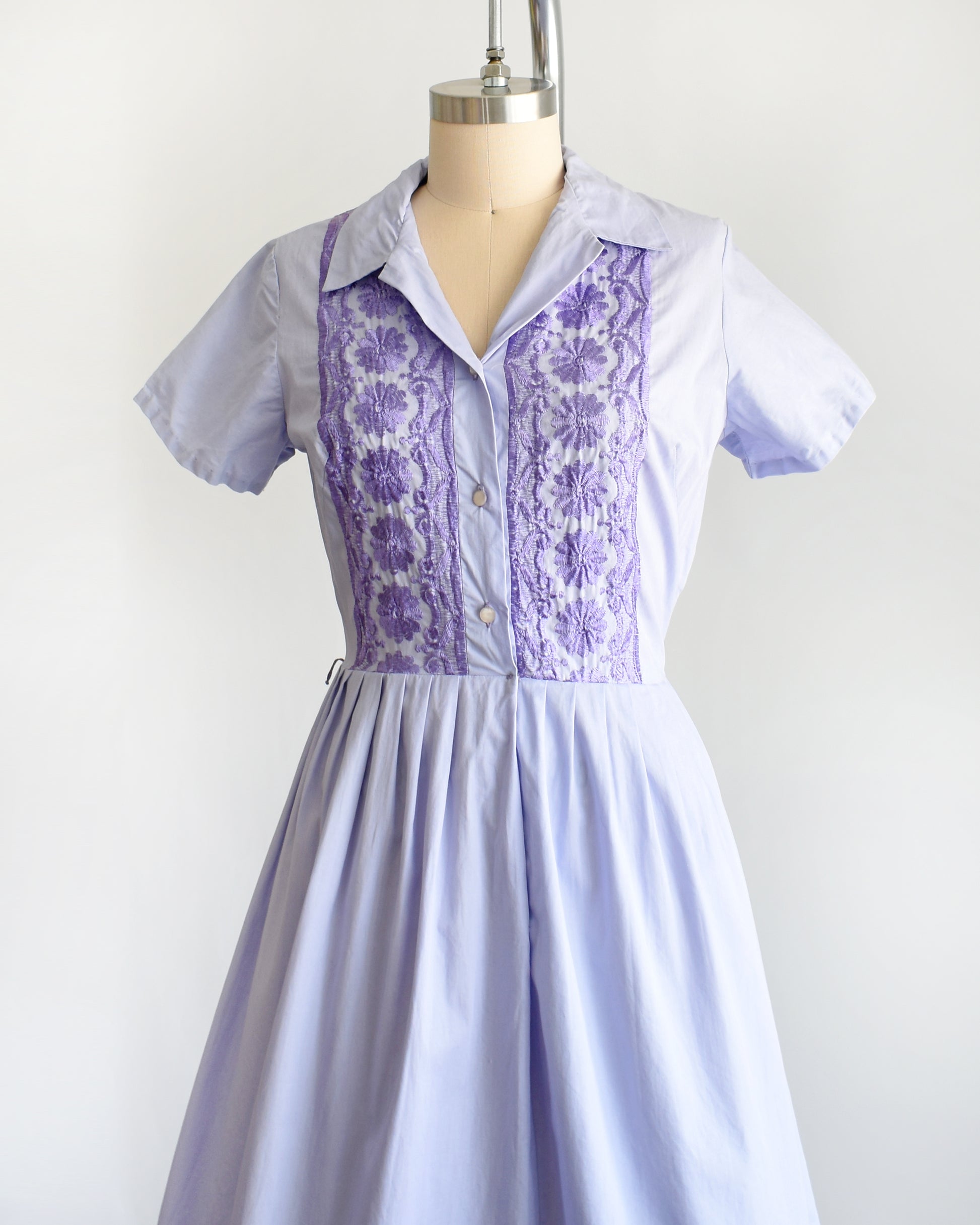 side front view of a vintage 1950s light purple dress with dark purple embroidery on a mannequin against a white background