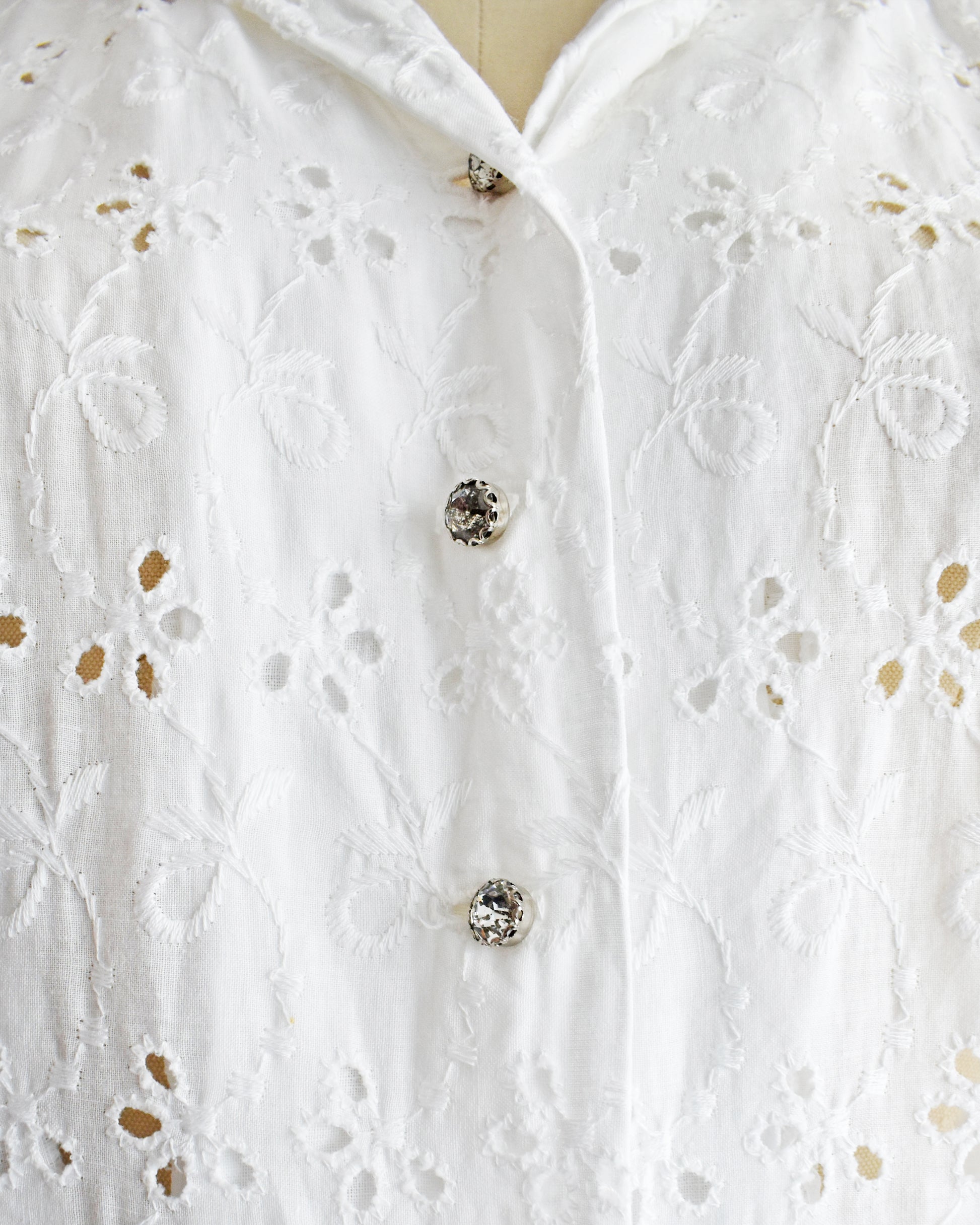close up of the rhinestone buttons and eyelet detail on a vintage 1950s white eyelet dress