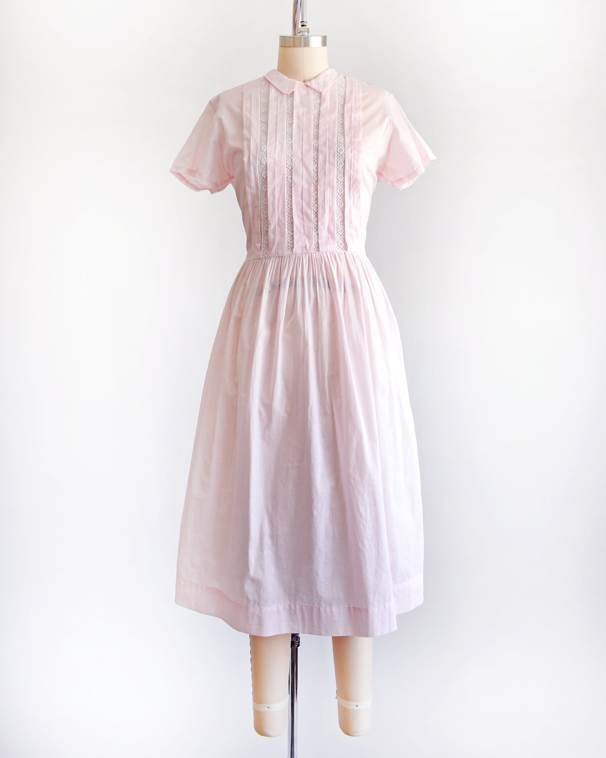 a vintage 1950s pink dress on a mannequin against a white background