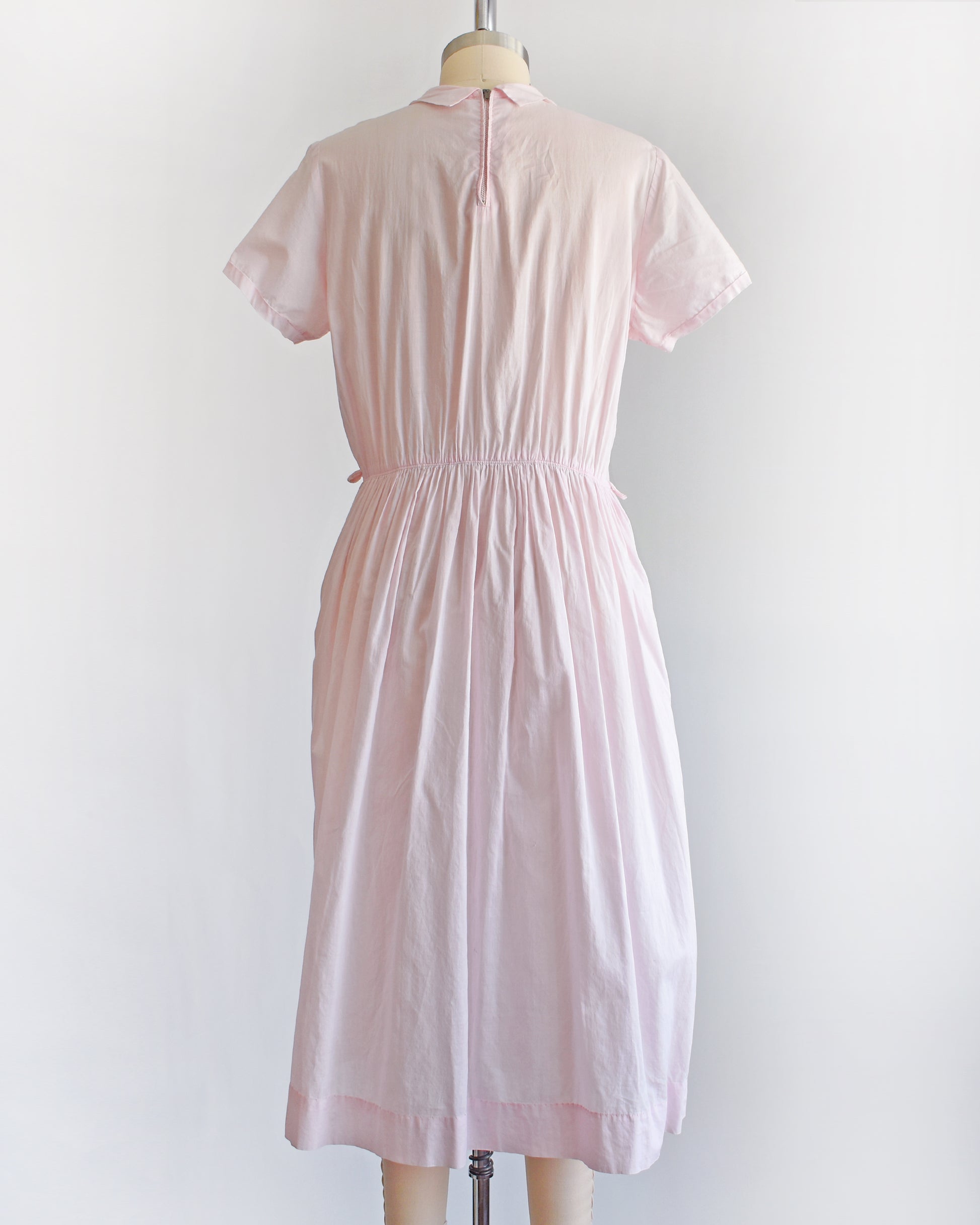 back view of a vintage 1950s pink dress on a mannequin against a white background