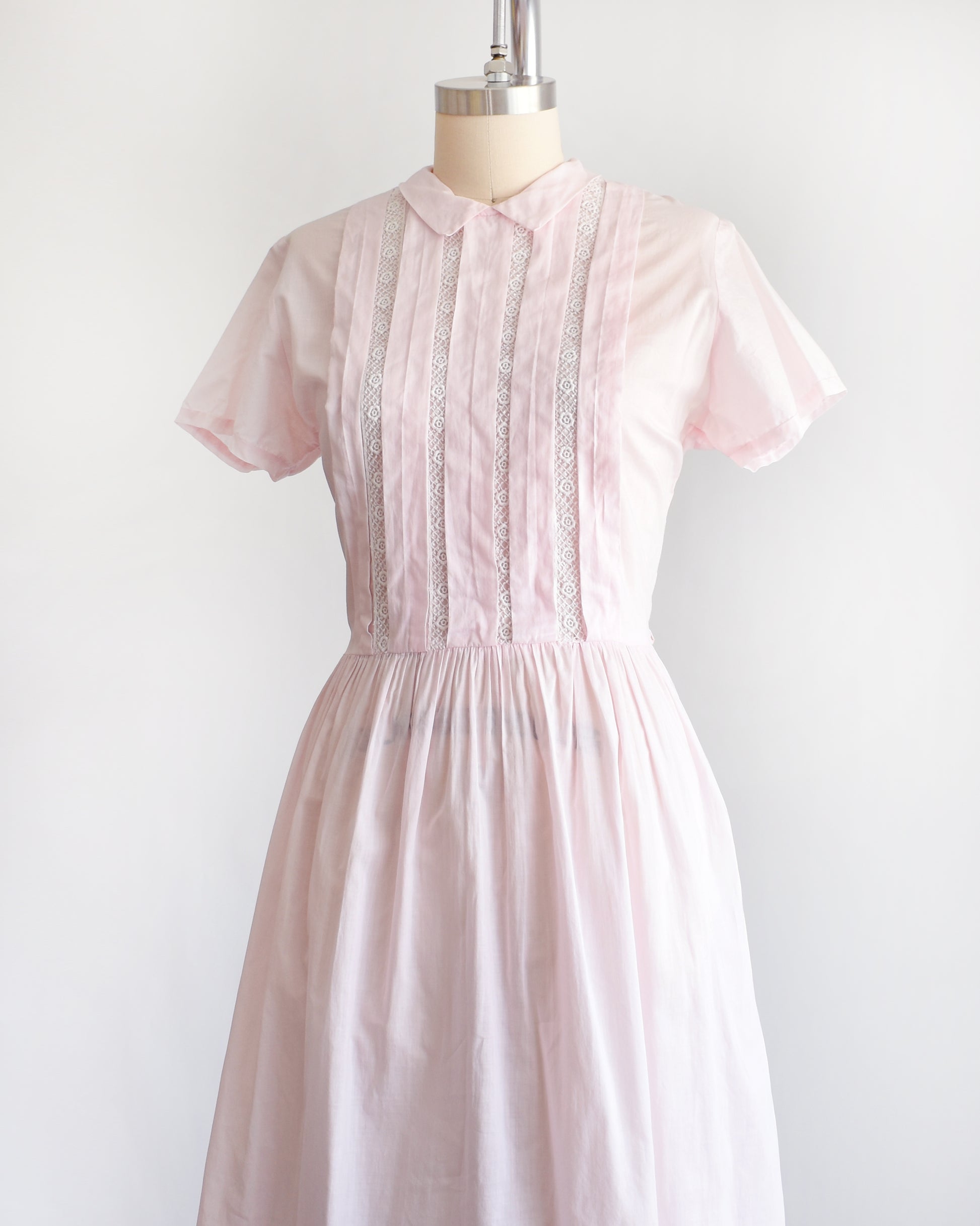 side front view of a vintage 1950s pink dress on a mannequin against a white background