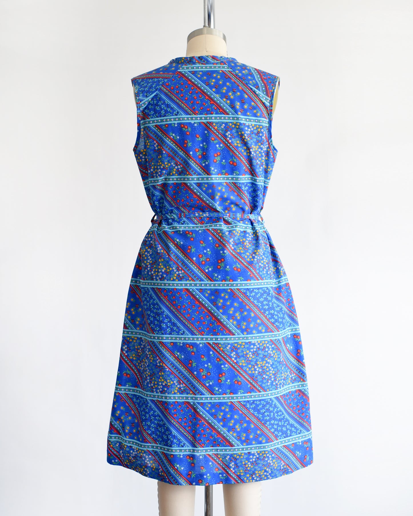 back view of a vintage 1970s blue floral dress on a mannequin against a white background