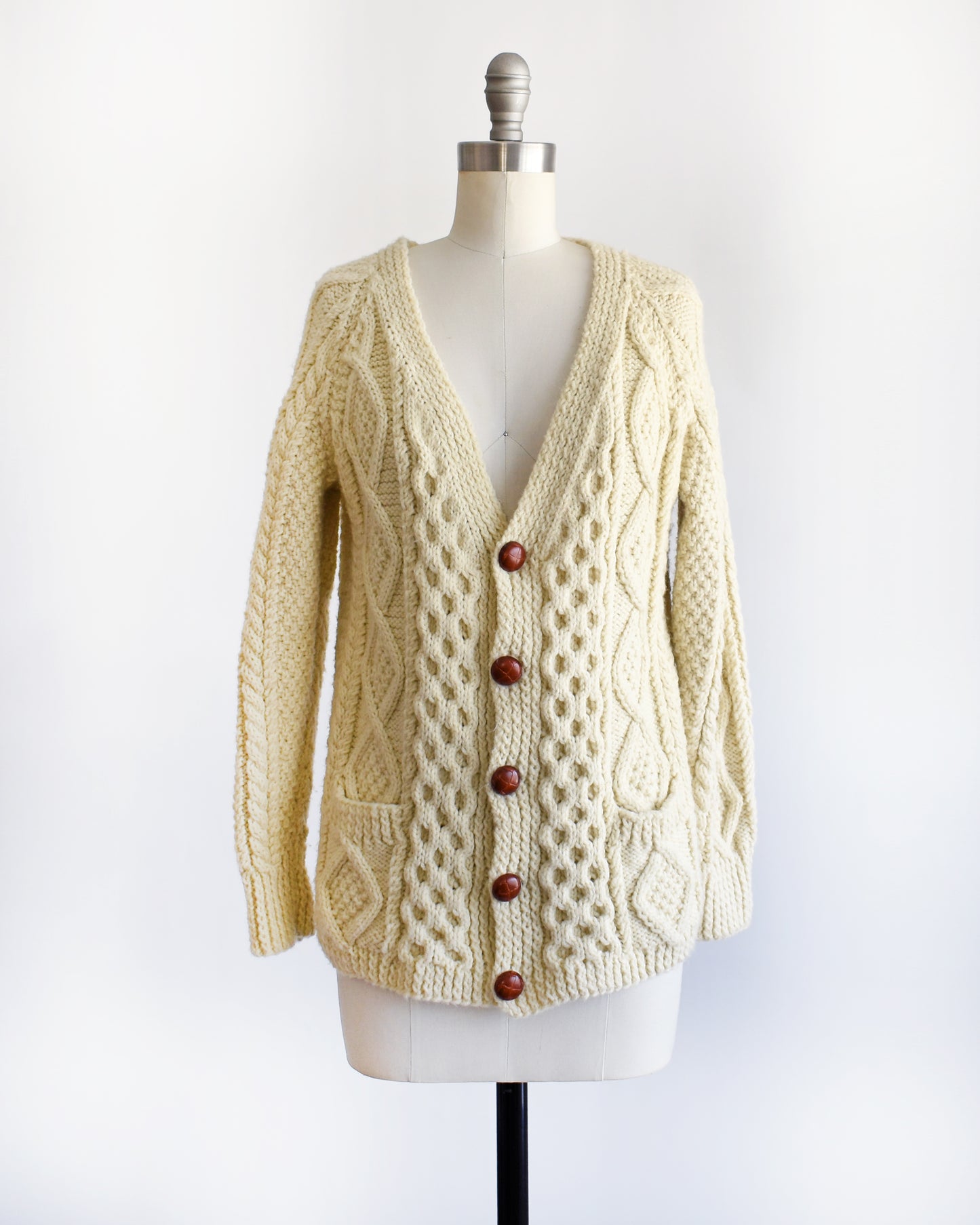 a vintage 1970s/1980s cream-colored cable knit cardigan on a mannequin against a white background