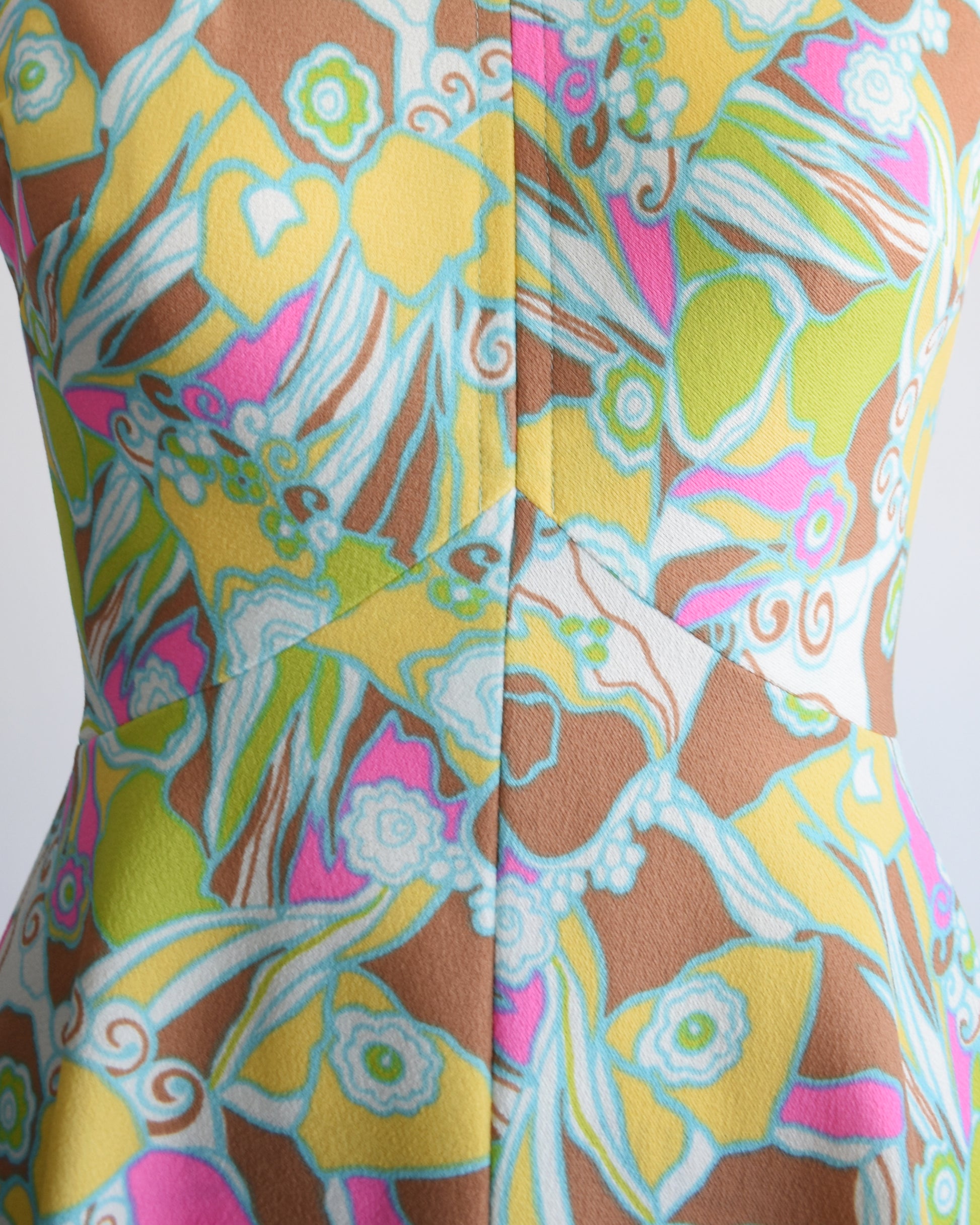 close up of the bodice on a vintage 1970s mod colorful floral dress on a mannequin against a white background
