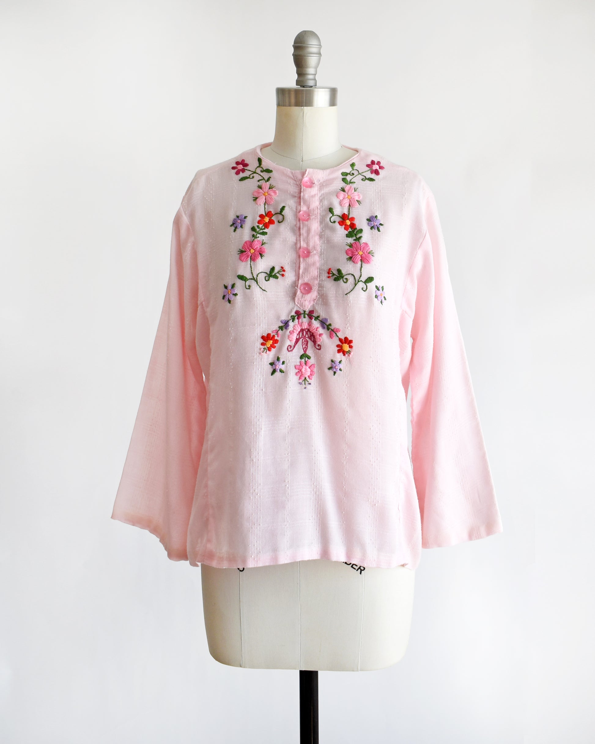 a vintage pink blouse with floral embroidery on a mannequin against a white background
