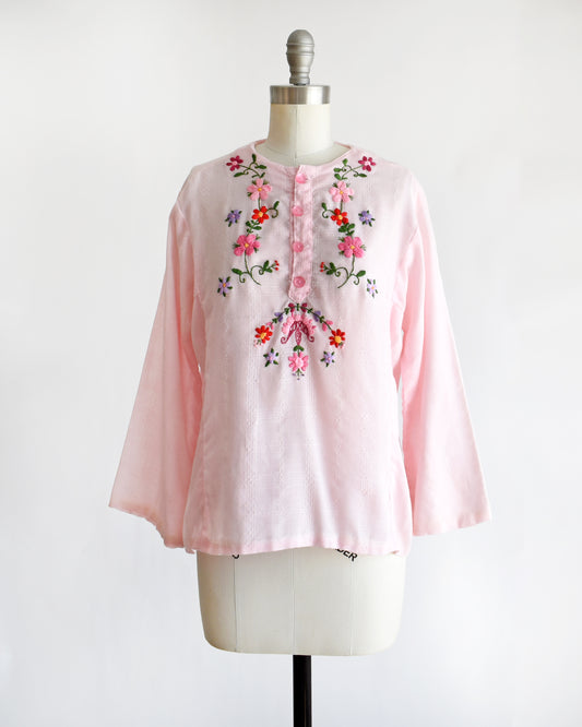 a vintage pink blouse with floral embroidery on a mannequin against a white background