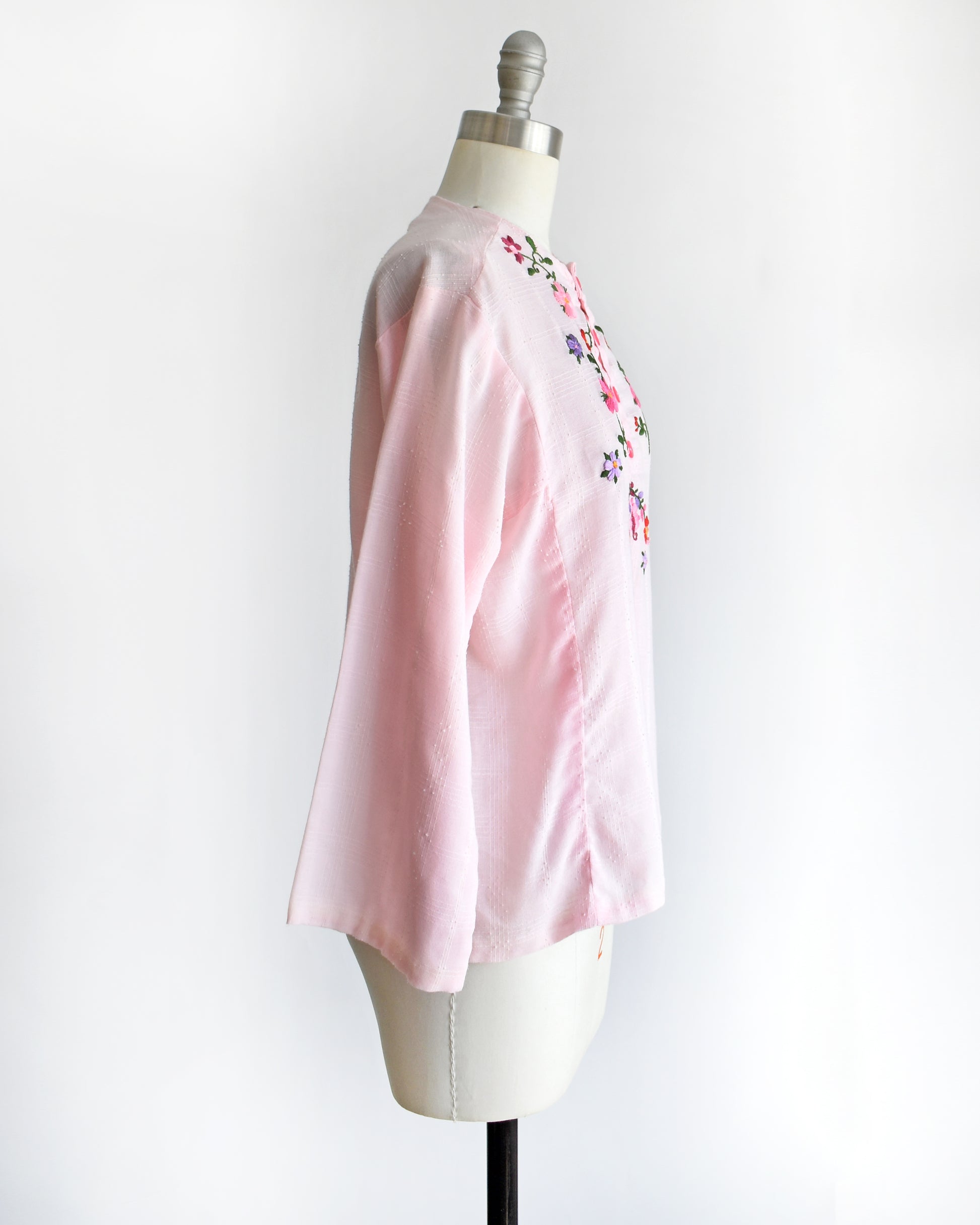 side view of a vintage pink blouse with floral embroidery on a mannequin against a white background