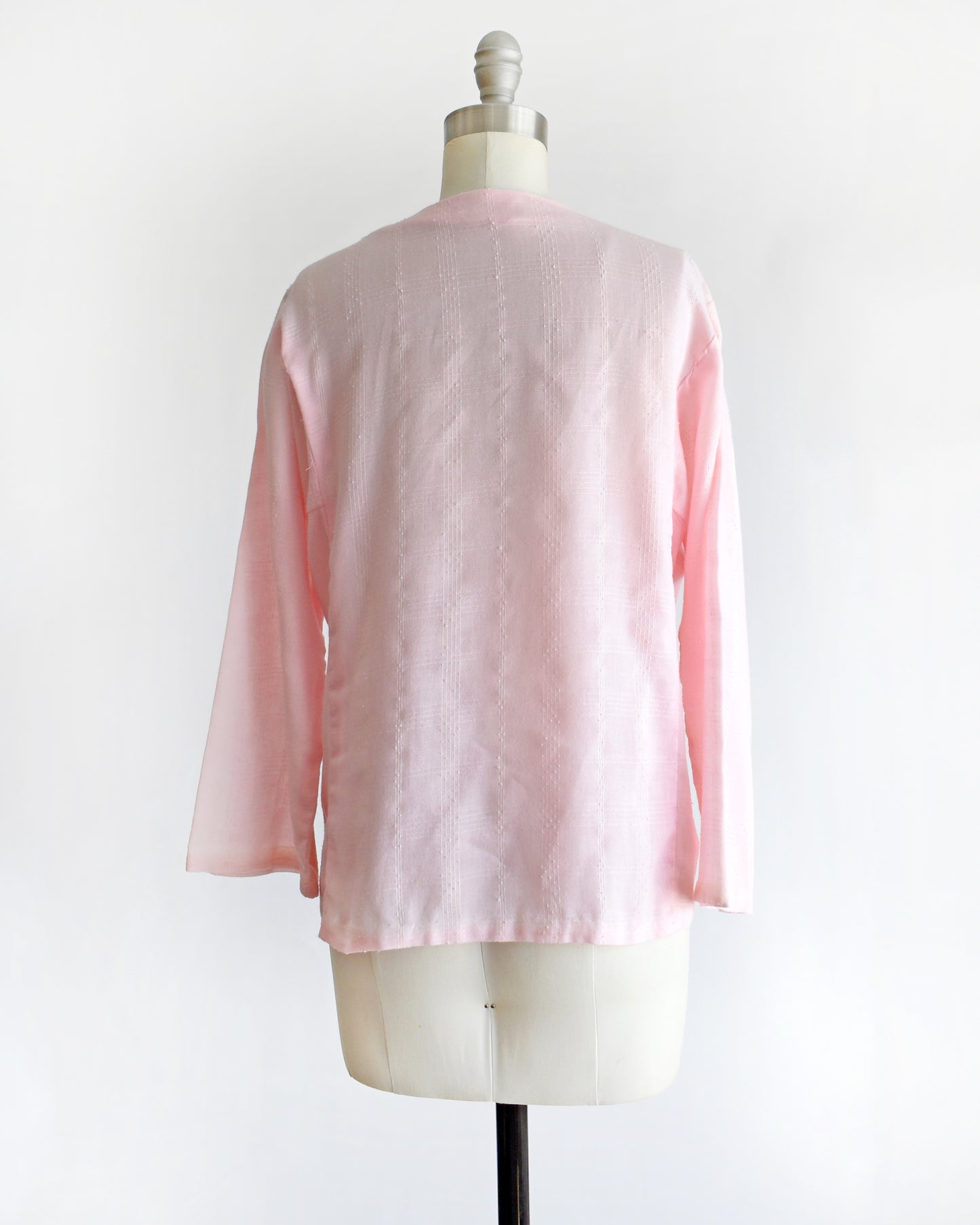 back view of a vintage pink blouse with floral embroidery on a mannequin against a white background
